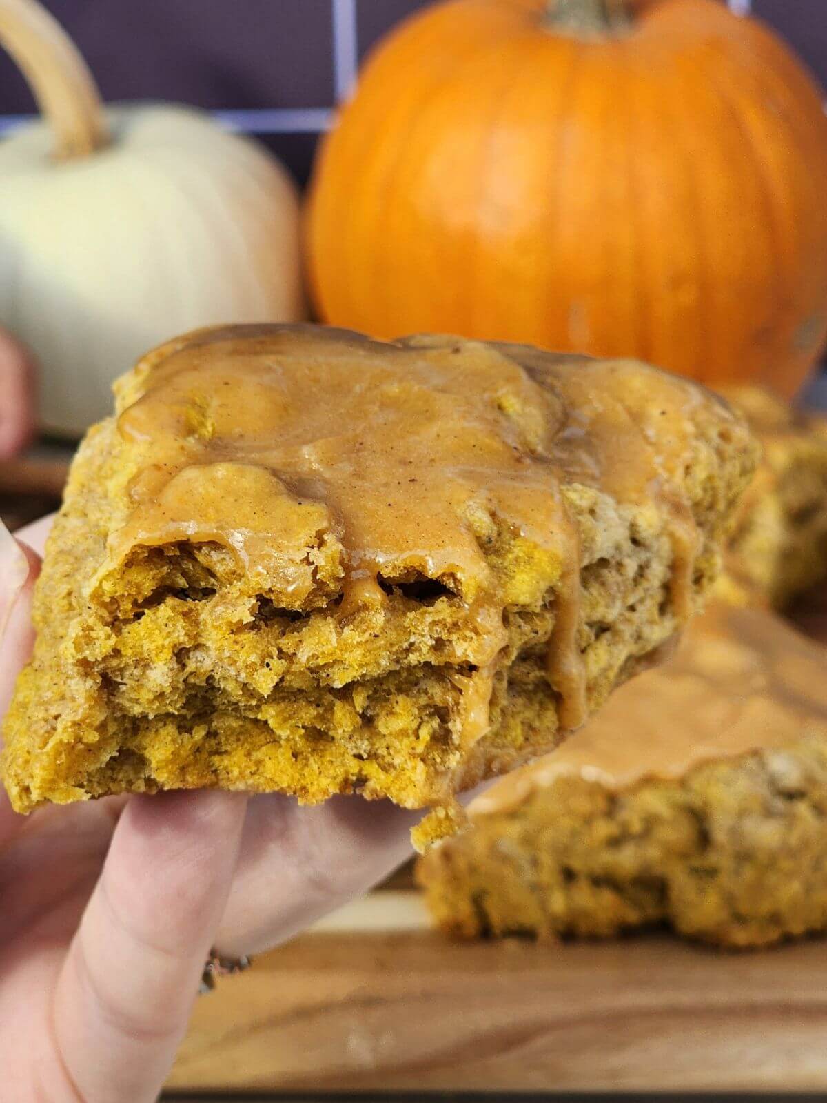 Close up of glazed pumpkin sourdough scones on a wooden board with pumpkins in the background.