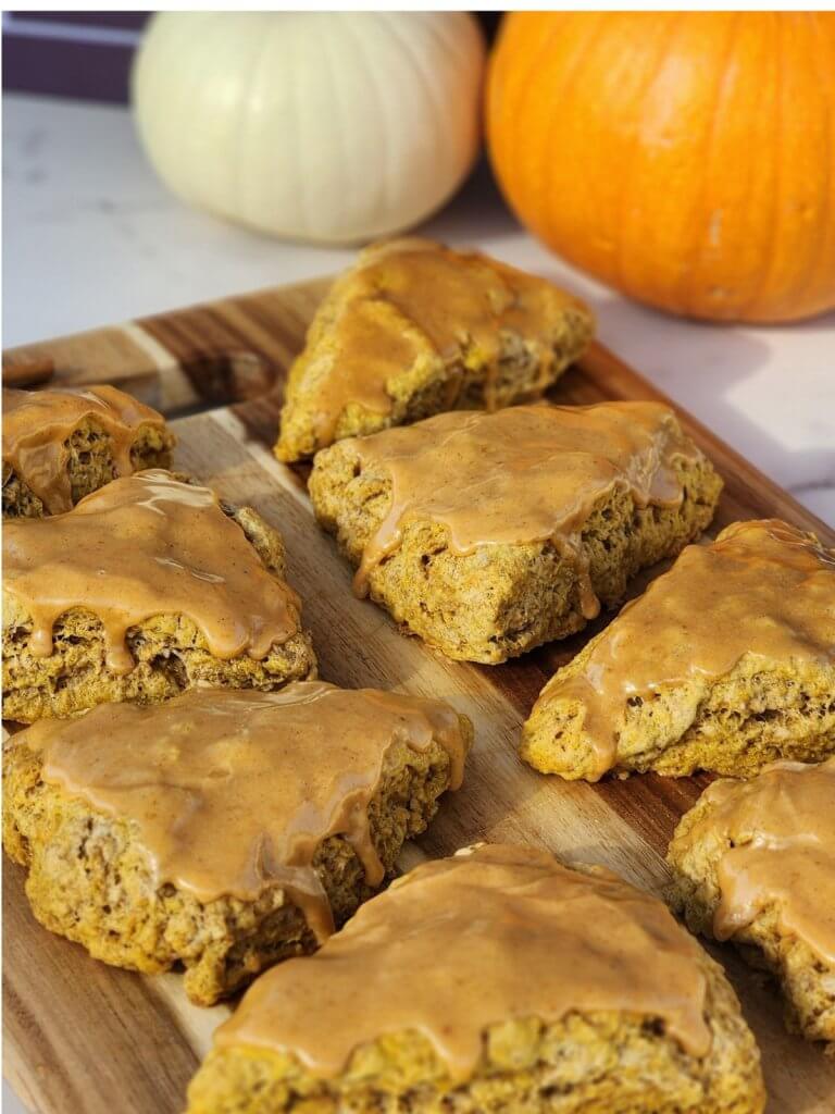 Pumpkin sourdough scones with maple glaze arranged on a wooden serving board.