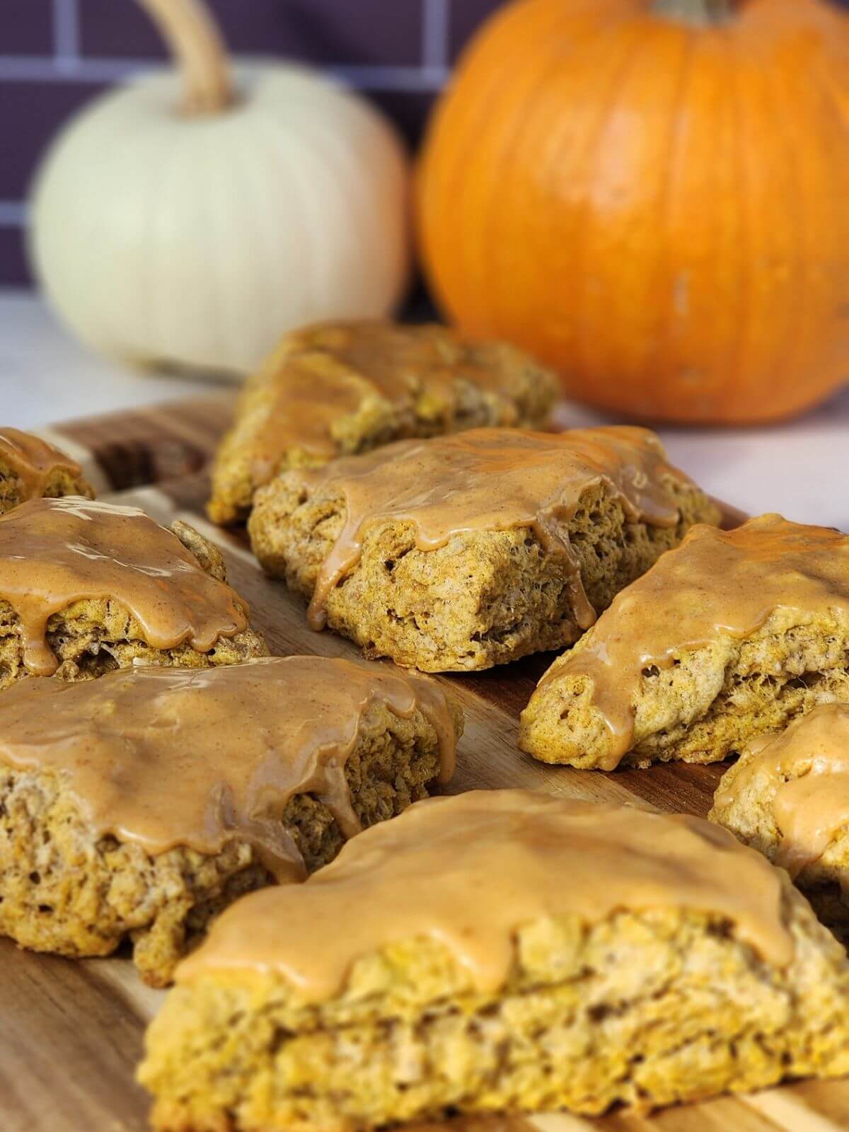 Close up of glazed pumpkin sourdough scones on a wooden board with pumpkins in the background.