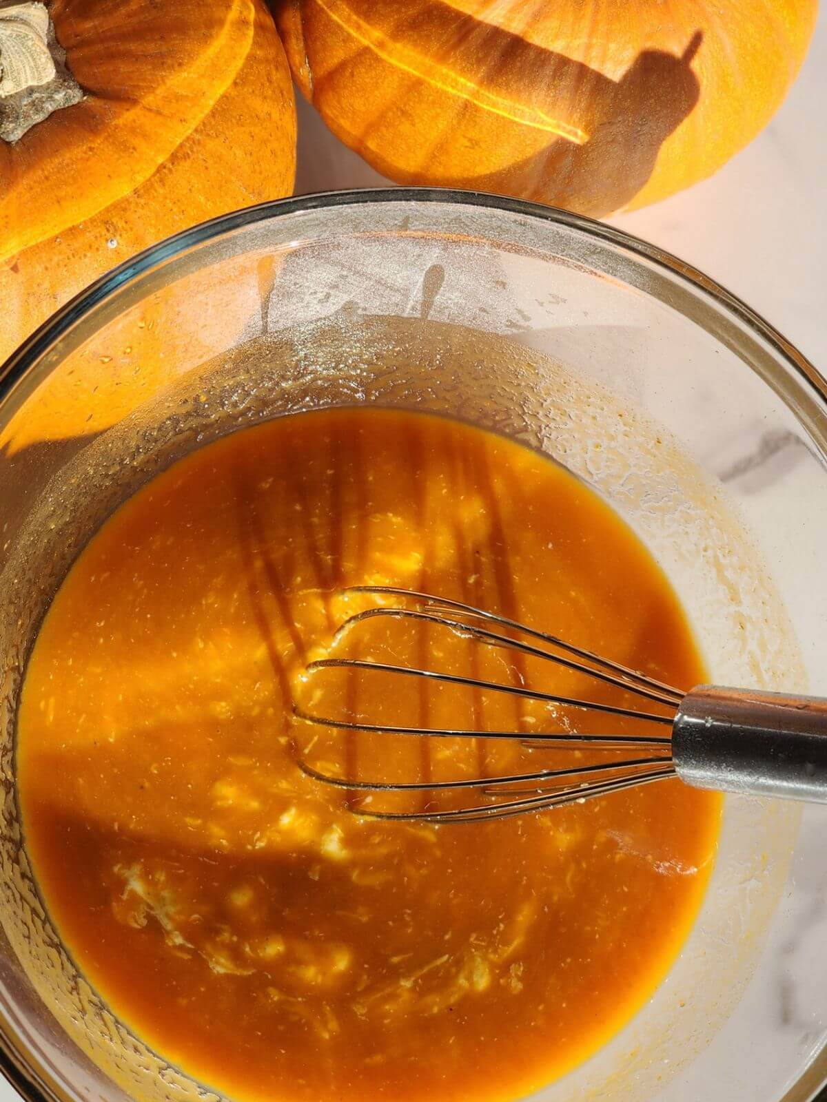 Pumpkin, sourdough starter, egg, and vanilla mixture whisked together in a glass bowl.
