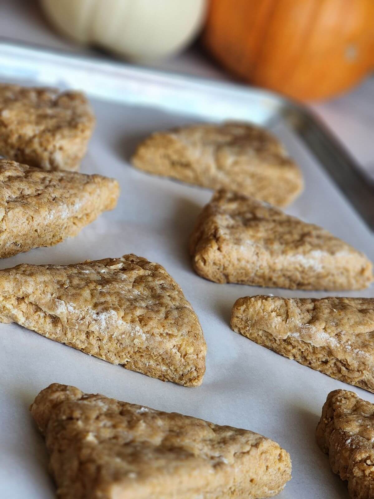 Unbaked pumpkin sourdough scones spaced on a parchment lined baking sheet.