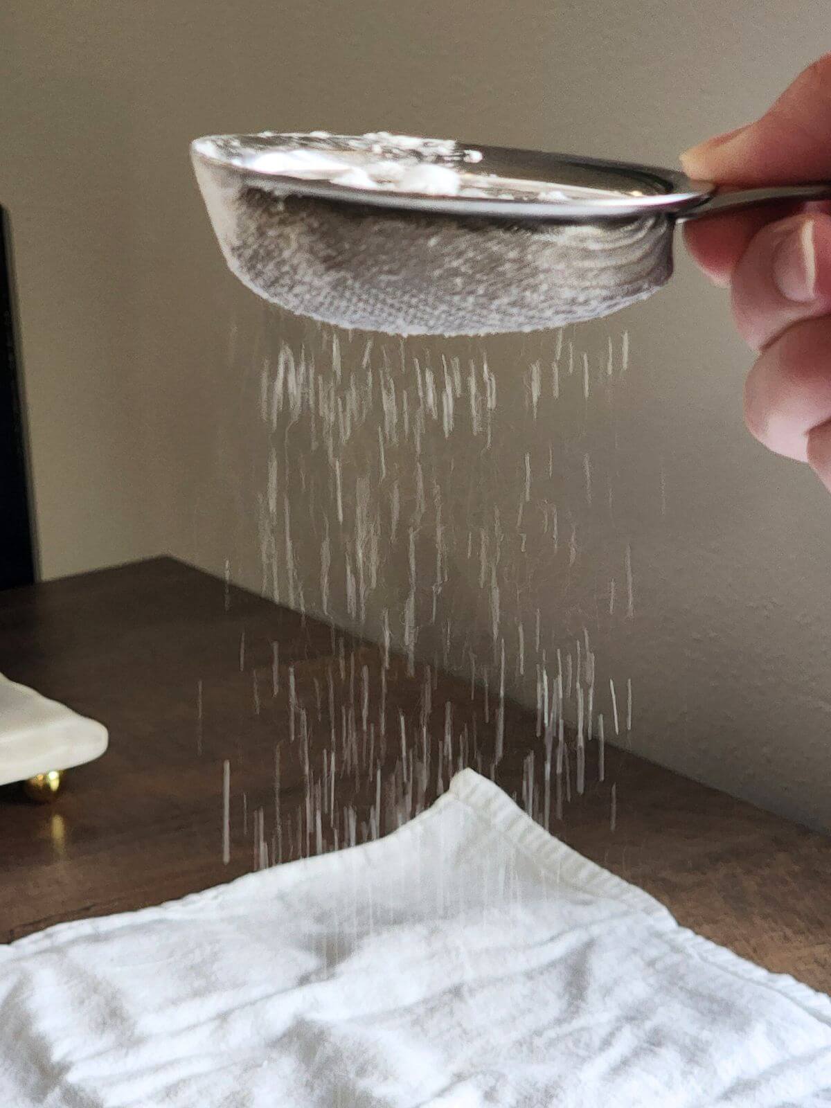Powdered sugar being sifted over a clean towel before rolling angel food cake.