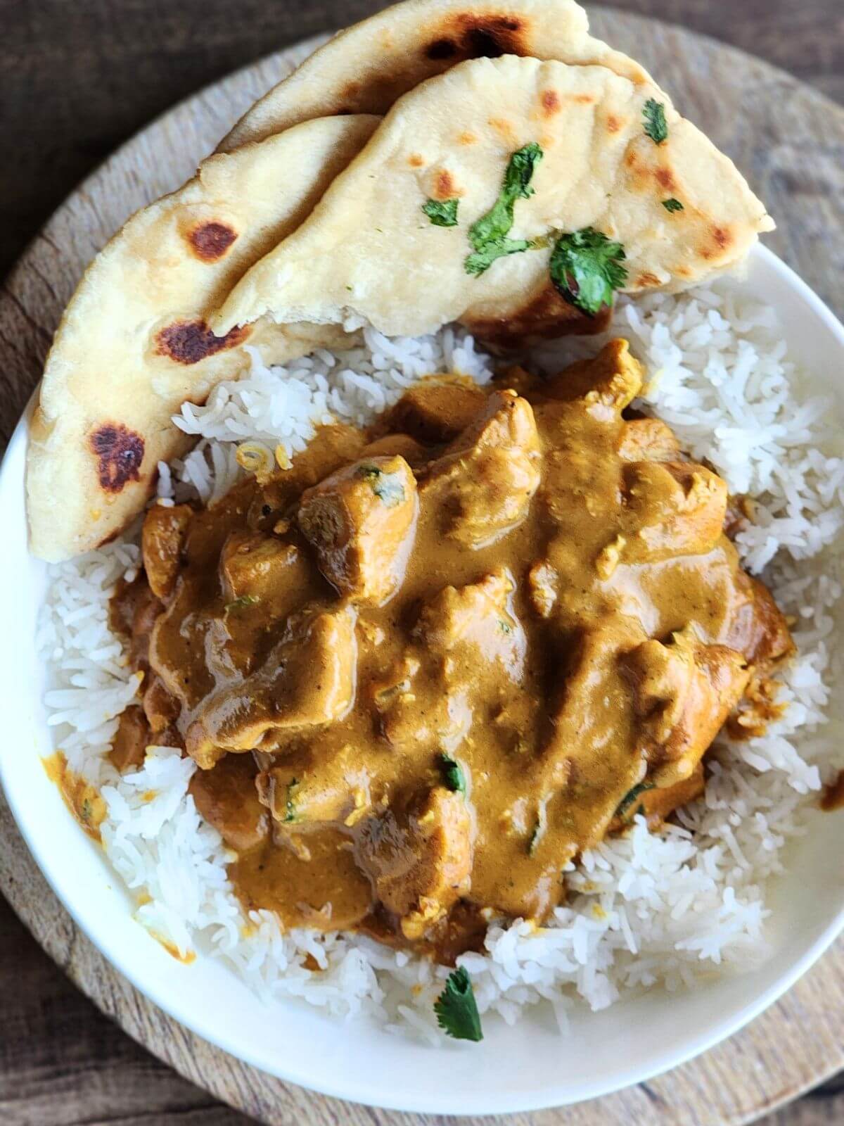 Butter chicken over rice with cilantro garnishes and naan on the side. 