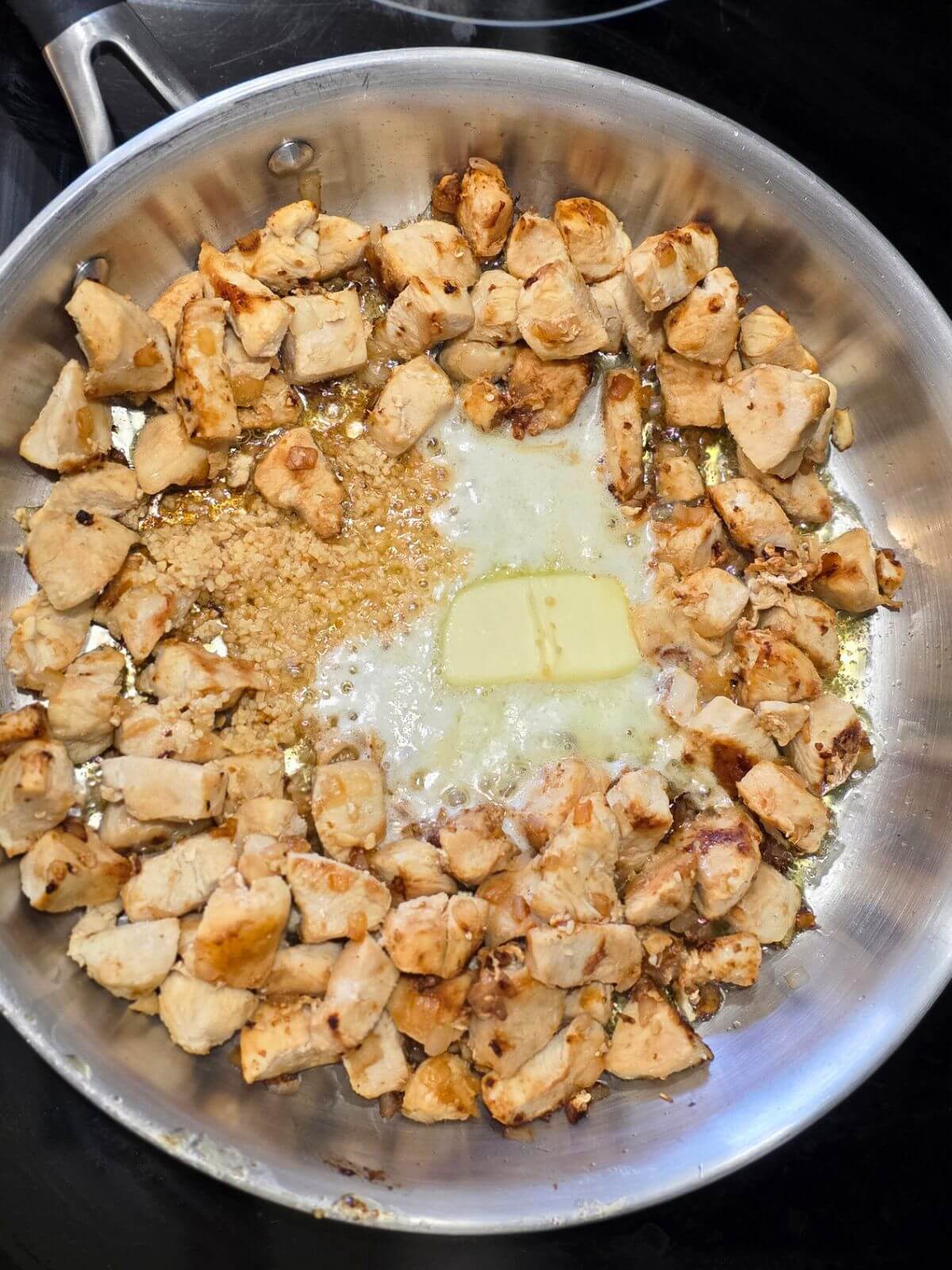 Pan of chicken sauteeing with butter  and garlic in the center.
