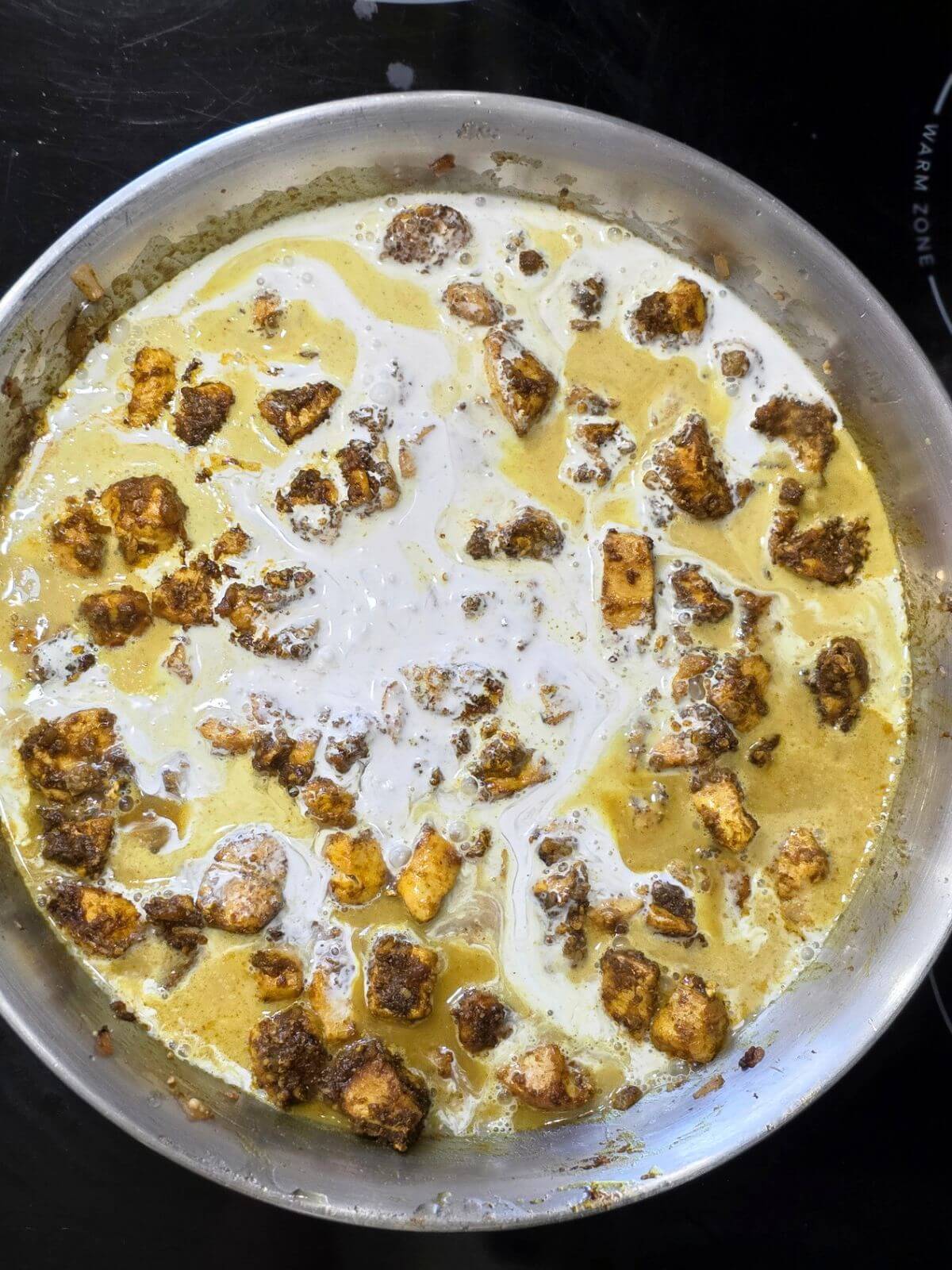 Coconut milk and cream added to butter chicken in skillet.