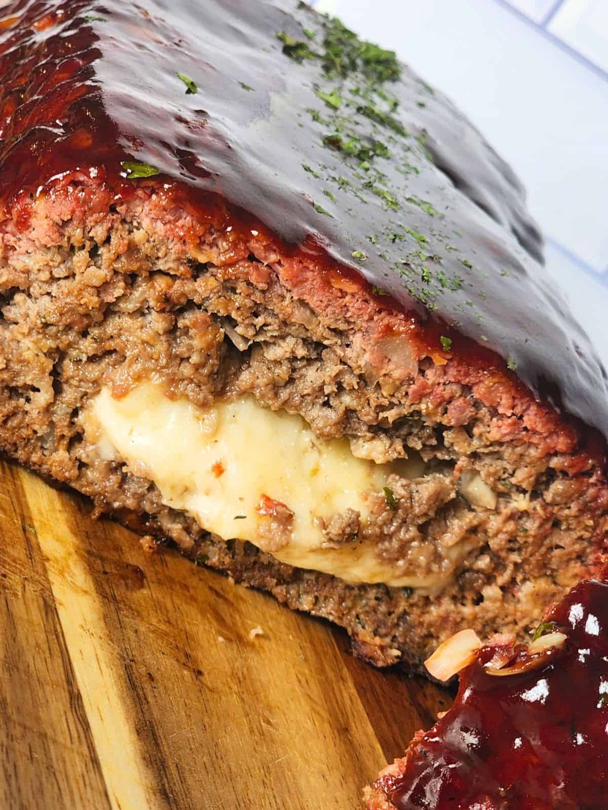 Close up of smoked meatloaf with BBQ sauce and melted cheese in the center.