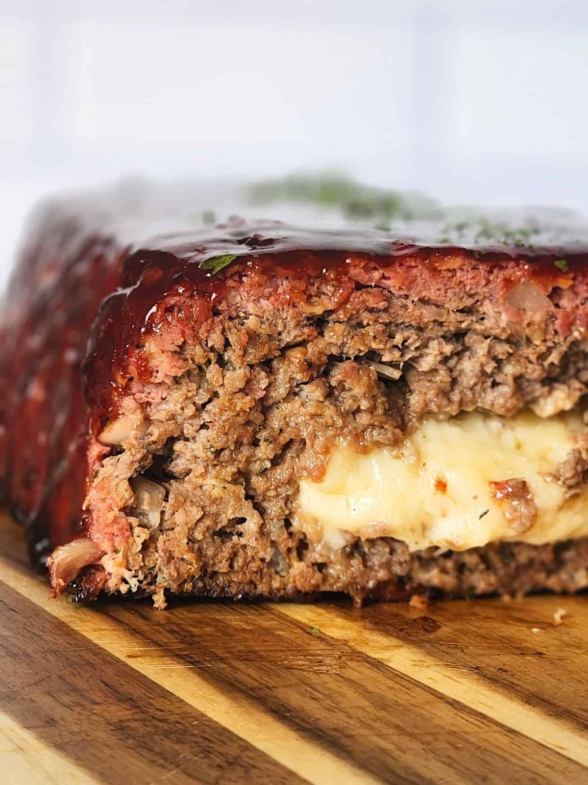 Sliced smoked meatloaf with a melted cheese center on a wooden cutting board.