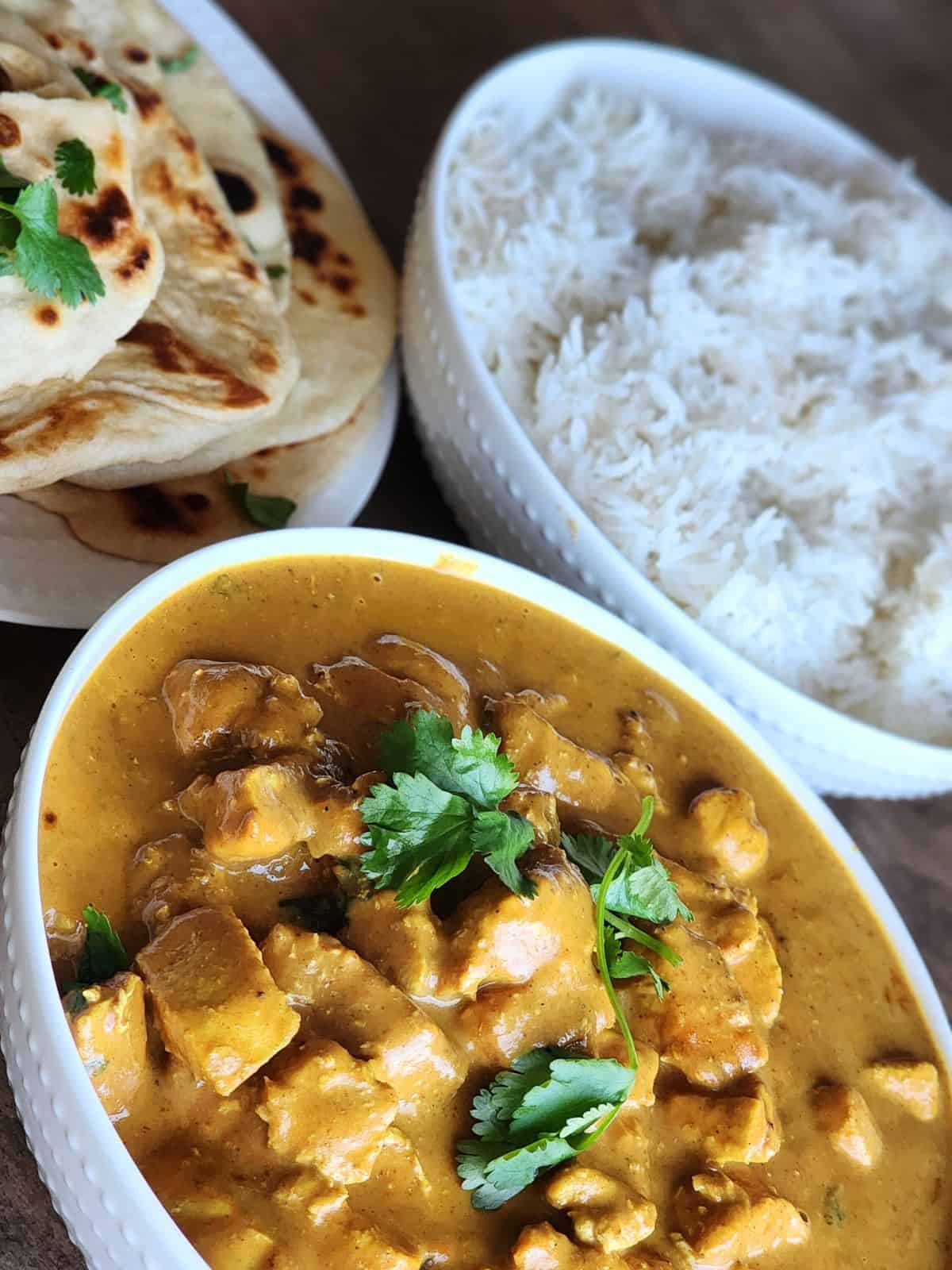 Three different bowls filled with Butter Chicken, rice, and naan. 