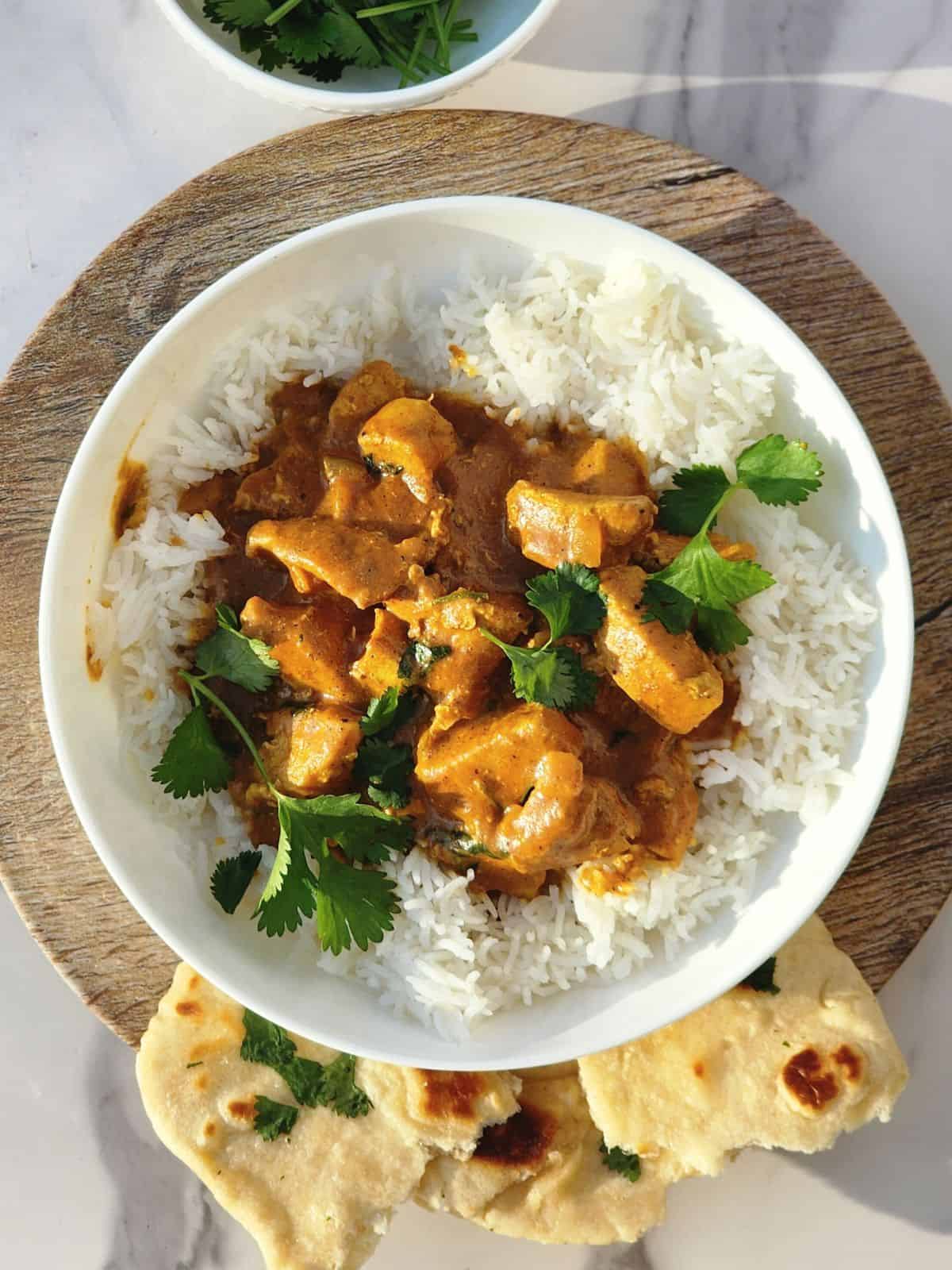 Butter chicken over rice with cilantro garnishes and naan on the side. 