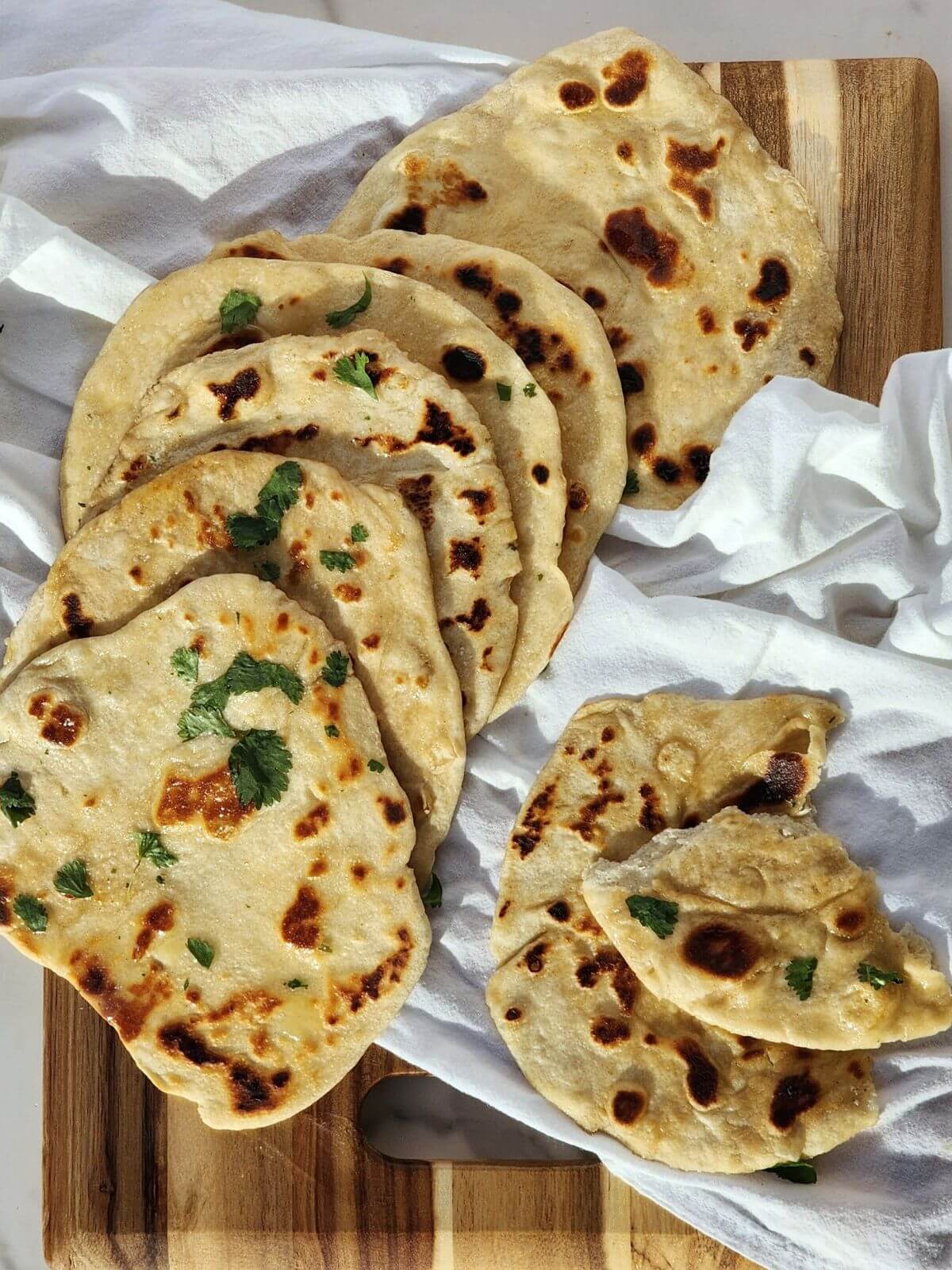 Sourdough naan bread laying on a white towel, one is ripped in pieces.