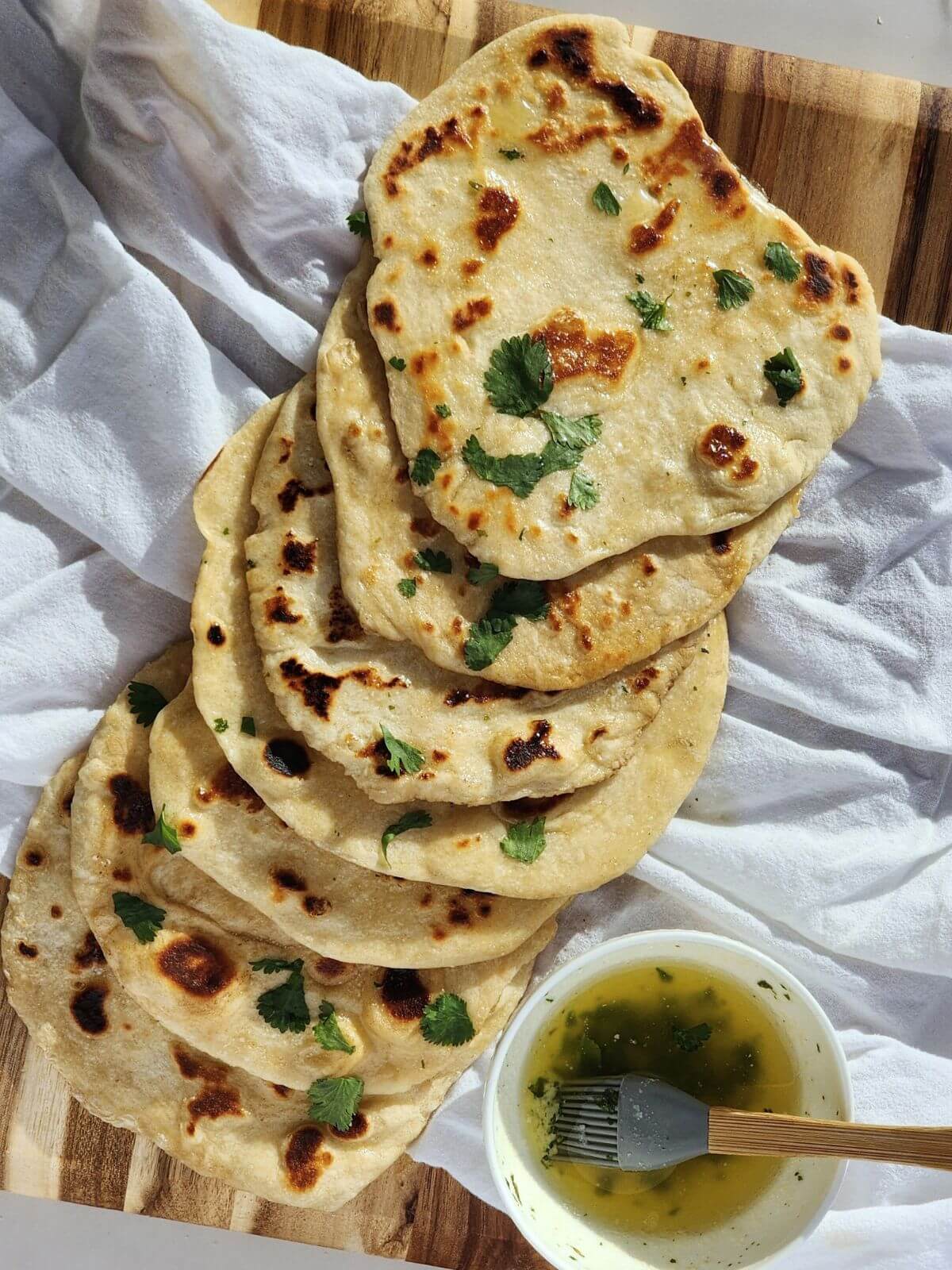 A stack of naan bread on a towel with a bowl of herby butter on the side.