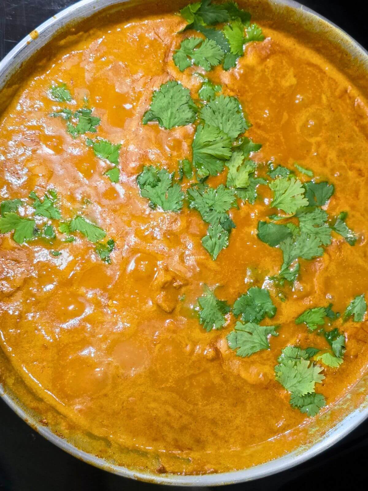 Butter chicken under sauce in a skillet topped with a sprinkle of cilantro.