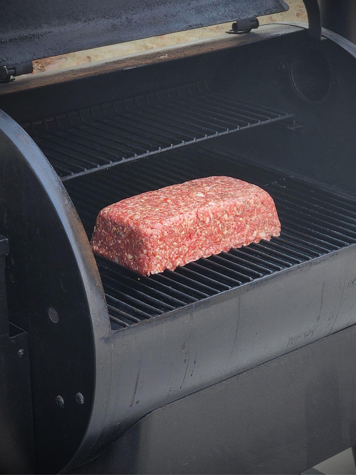 Raw shaped meatloaf placed directly on a smoker rack for a smoked meatloaf recipe with cheese.