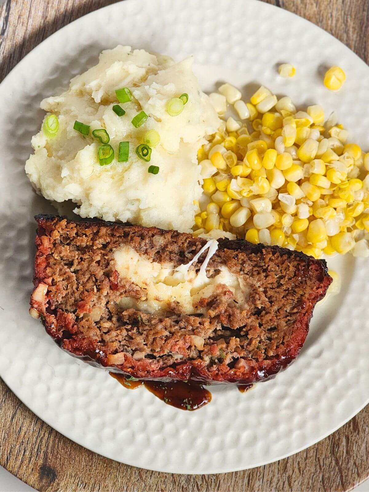 Slice of smoked meatloaf with melted cheese served with mashed potatoes and corn.