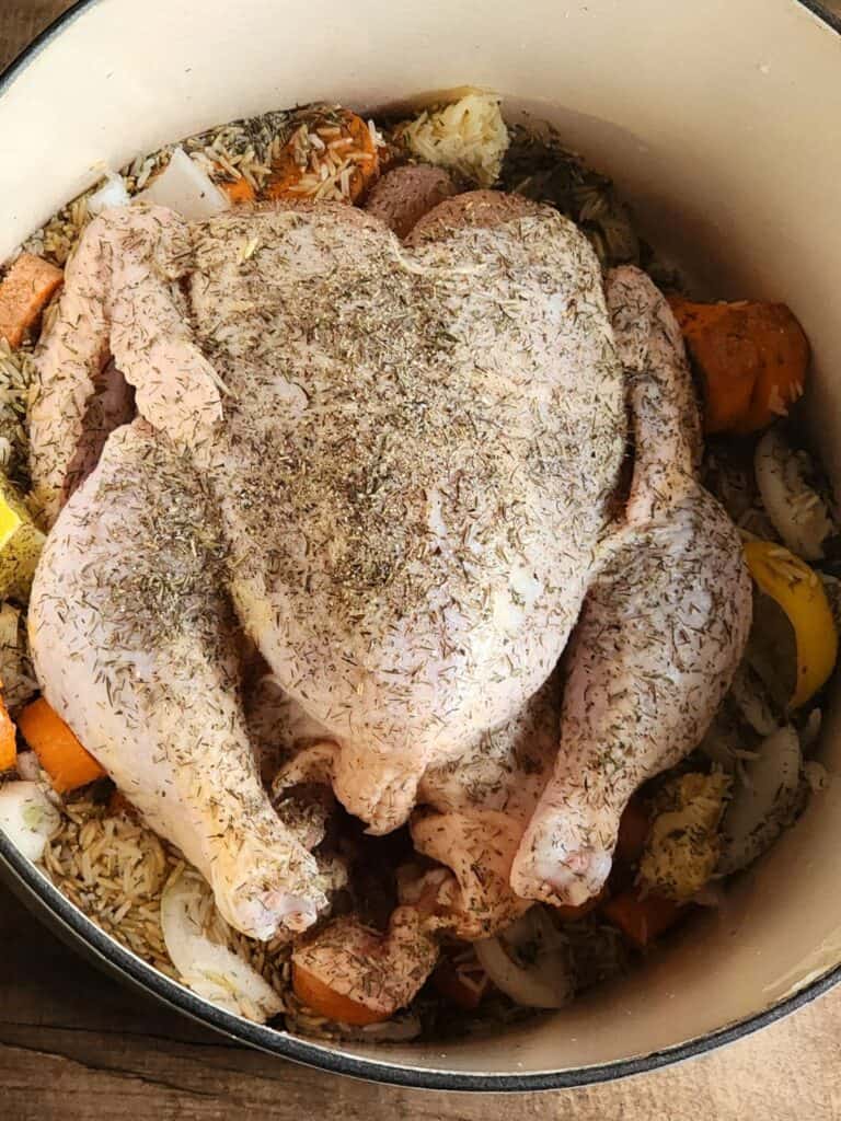 uncooked whole chicken on top of rice grains and other ingredients