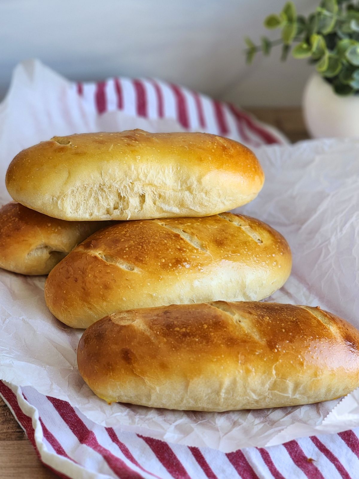 Stacked sourdough hoagie rolls on parchment paper and a striped towel.