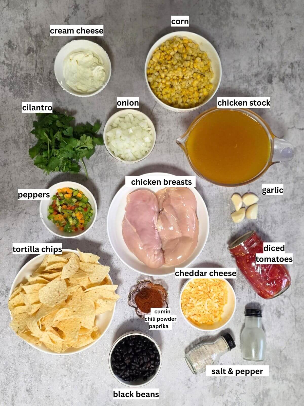 Fresh ingredients for cheesy chicken tortilla soup arranged on a rustic wooden kitchen counter.