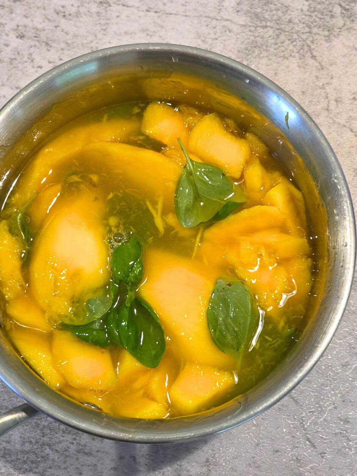 Fresh mango and basil simmering in a saucepan for homemade mango syrup.