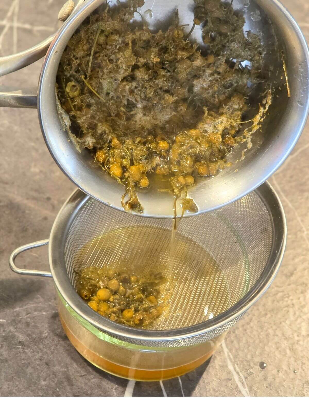 Straining chamomile honey syrup.