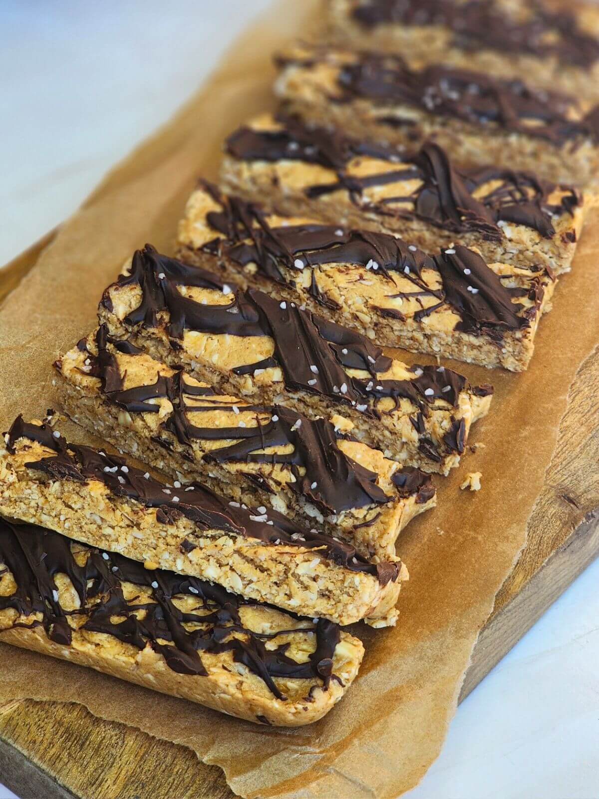 Sliced chocolate coconut protein bars arranged on parchment paper with chocolate drizzle and sea salt.