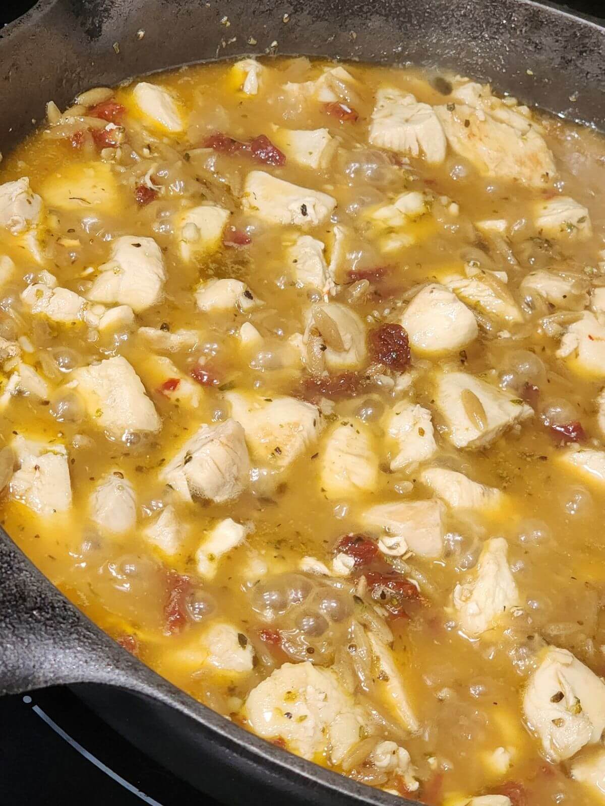 Chicken pieces cook in a skillet with sun dried tomatoes and broth.