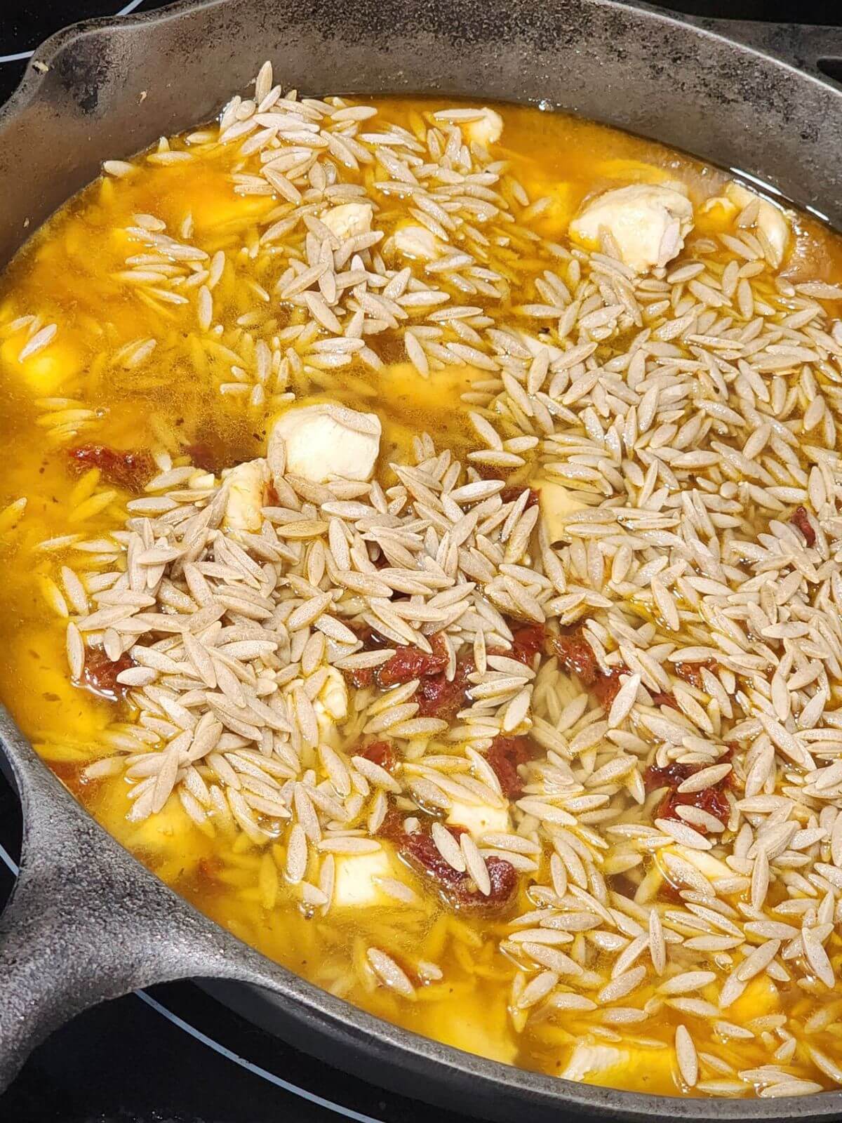 Dry orzo is added to a skillet with chicken, broth, and sun dried tomatoes.