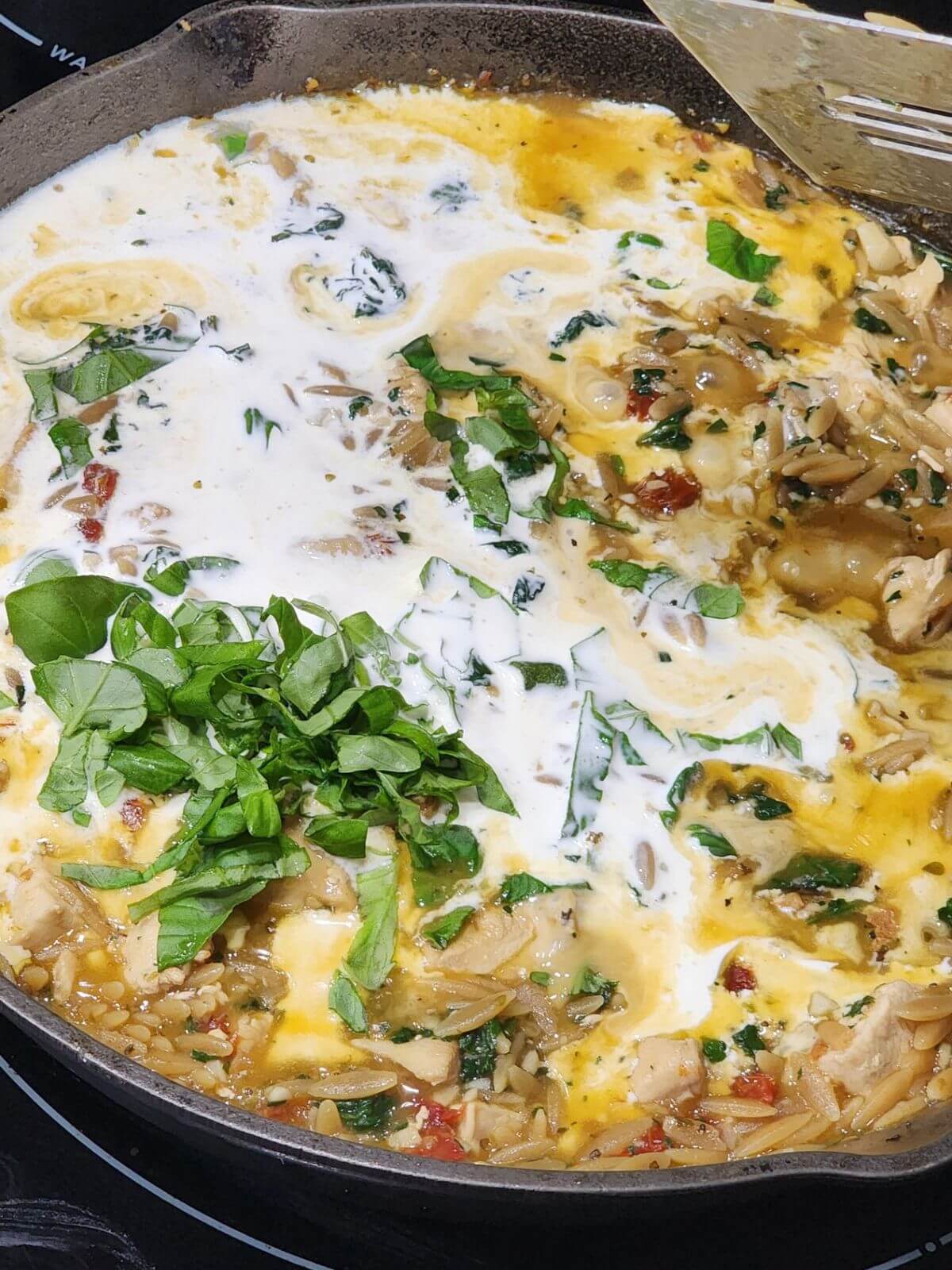 Cream is poured into a skillet with chicken, orzo, spinach, and basil.