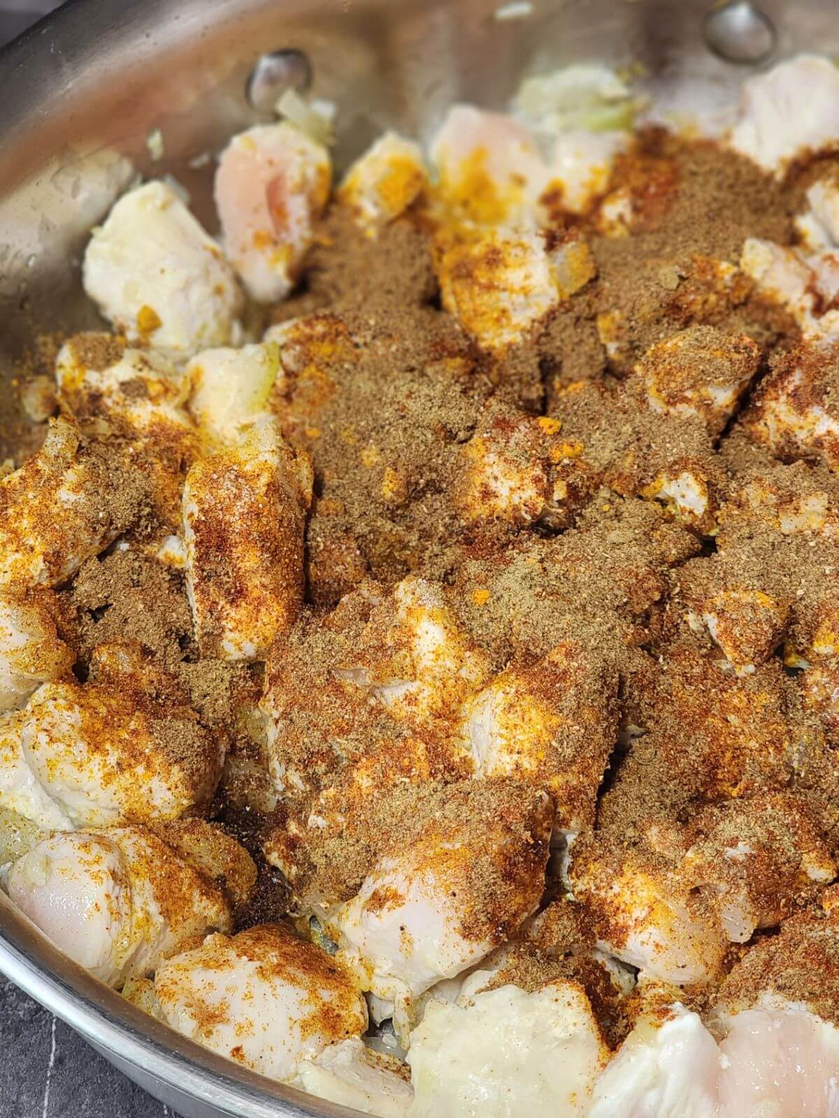 Chicken pieces cooking with onion, garlic, and warm tikka masala spices.
