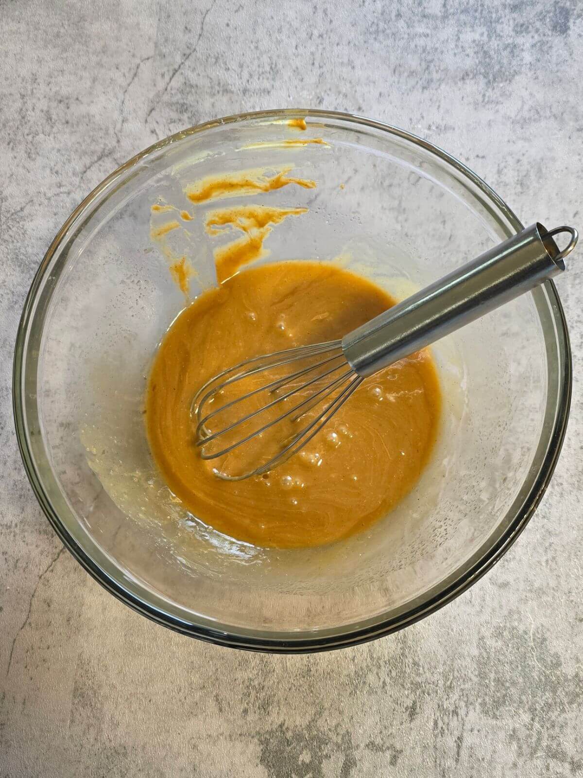 Peanut butter, honey, coconut oil, and vanilla whisked together in a glass mixing bowl.