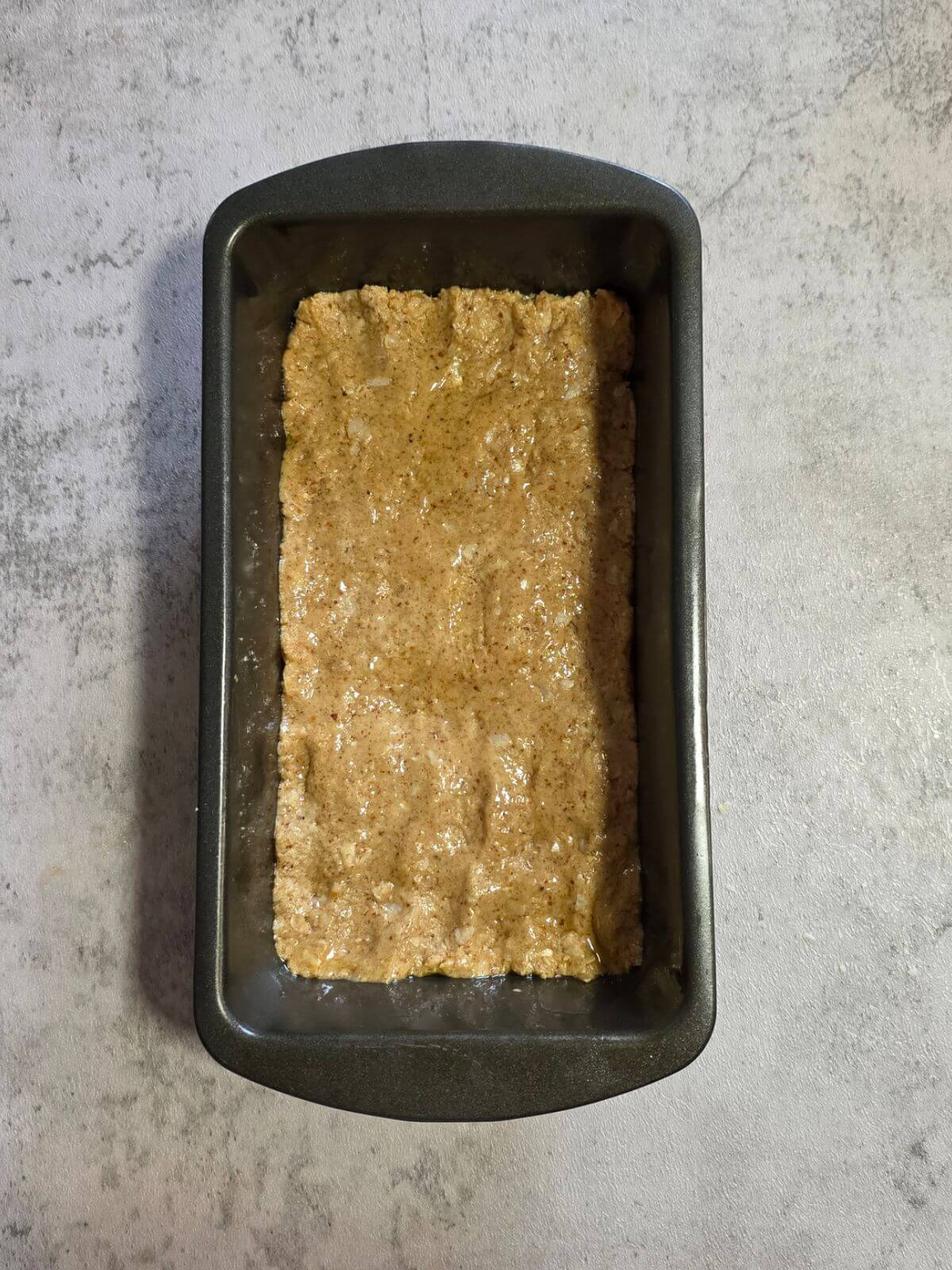 Chocolate coconut protein bar mixture pressed evenly into a loaf pan.