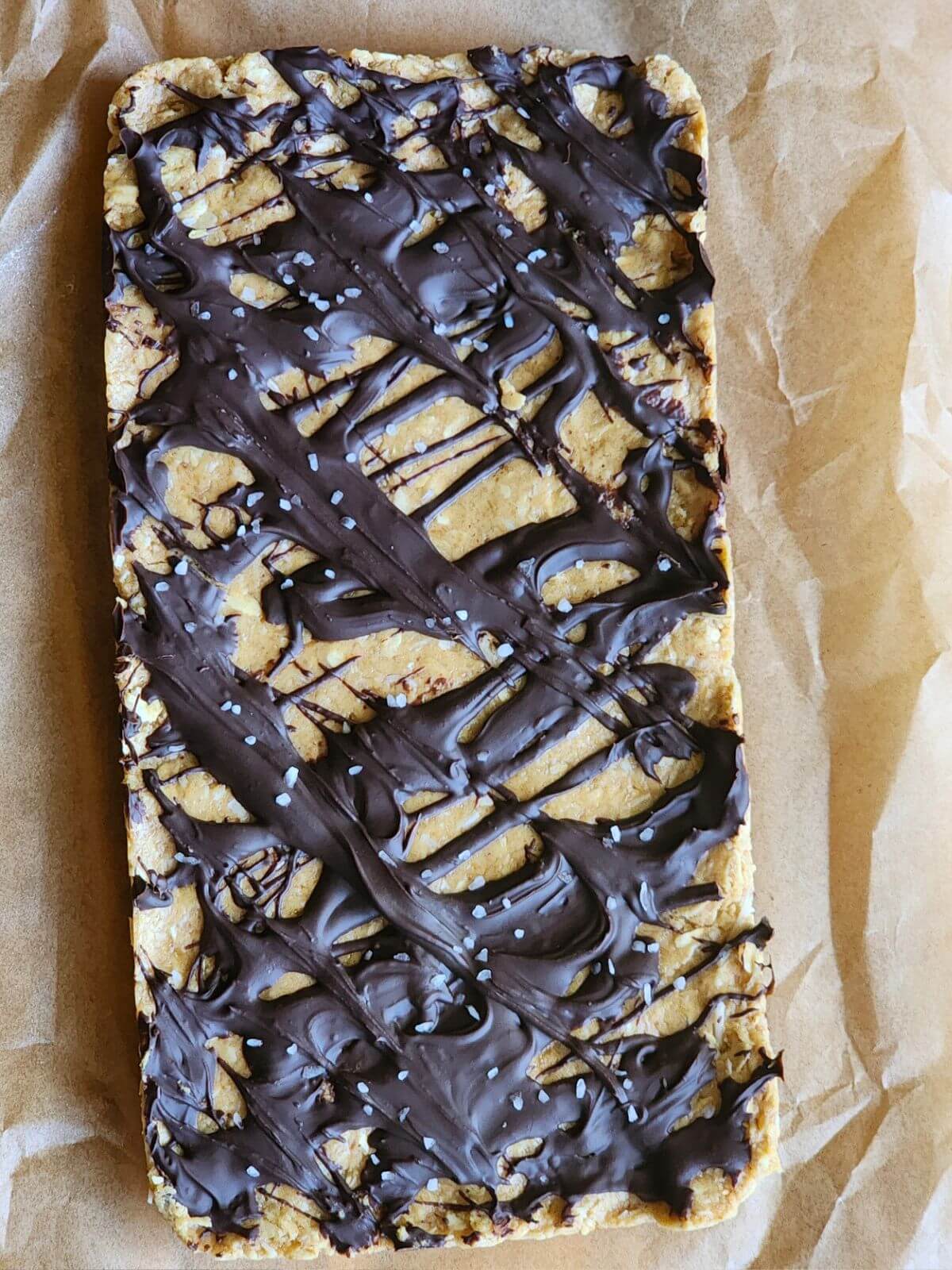 Uncut chocolate coconut protein bars topped with melted chocolate and flaky sea salt.