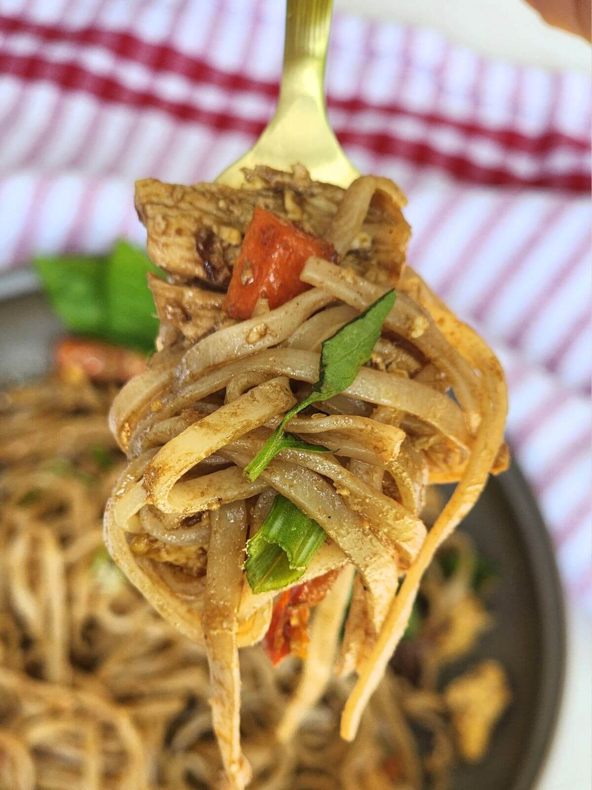 Forkful of easy chicken Pad Thai with tender chicken, rice noodles, red bell pepper, carrots, and fresh basil.