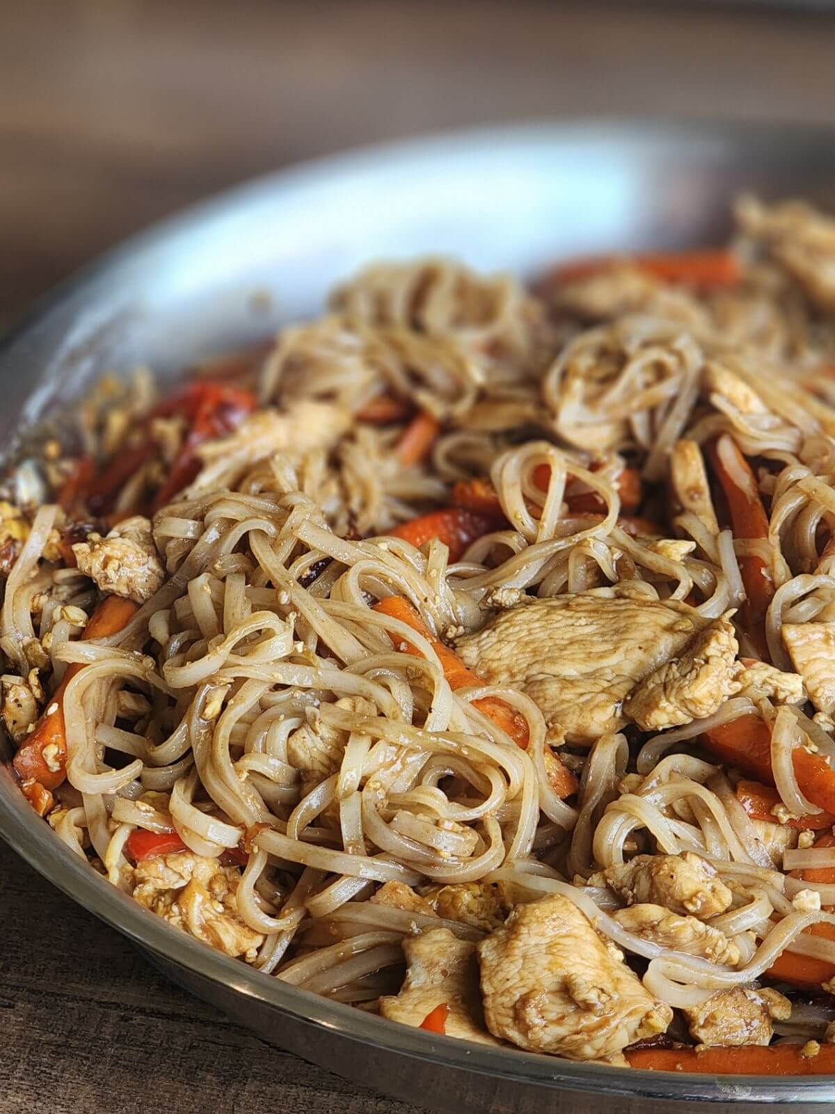 Skillet of homemade chicken Pad Thai with rice noodles, chicken, carrots, and red bell pepper.
