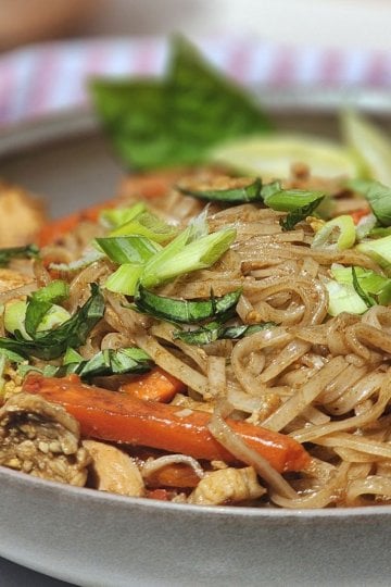 Easy chicken Pad Thai served in a bowl with chicken, rice noodles, carrots, red bell pepper, green onions, basil, and lime.