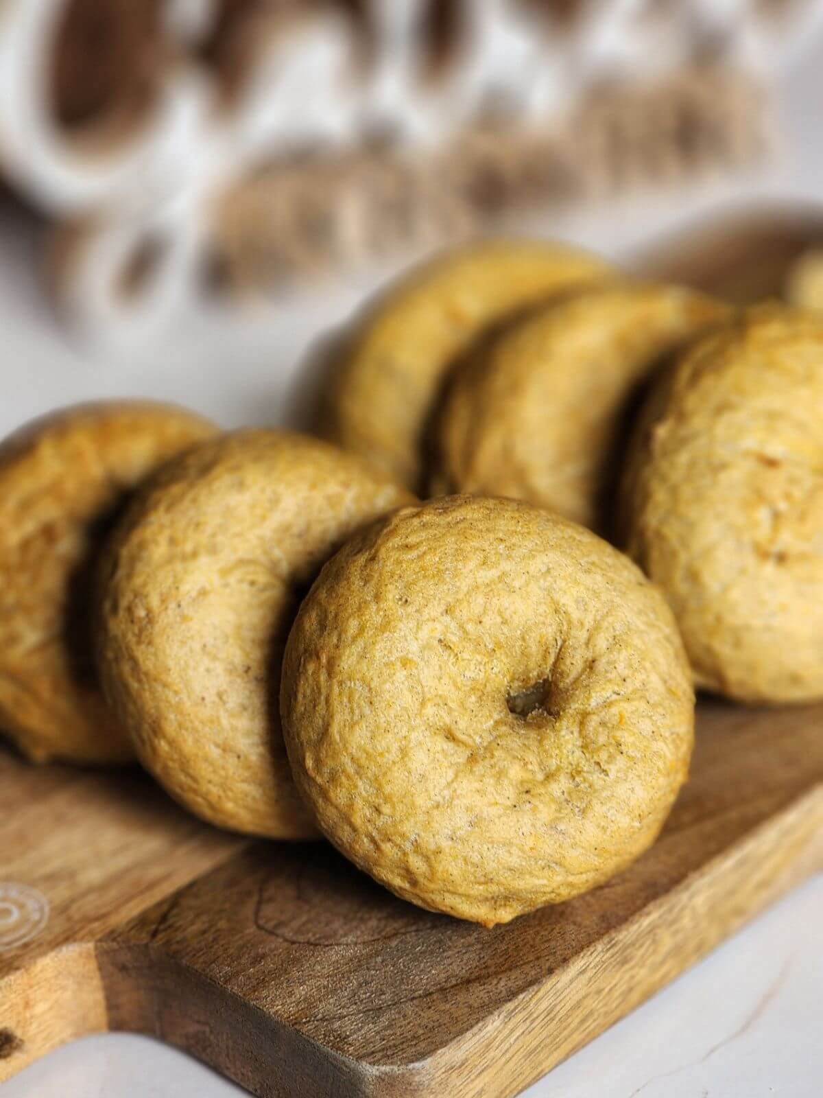 Homemade sourdough pumpkin bagels arranged on a wooden cutting board.