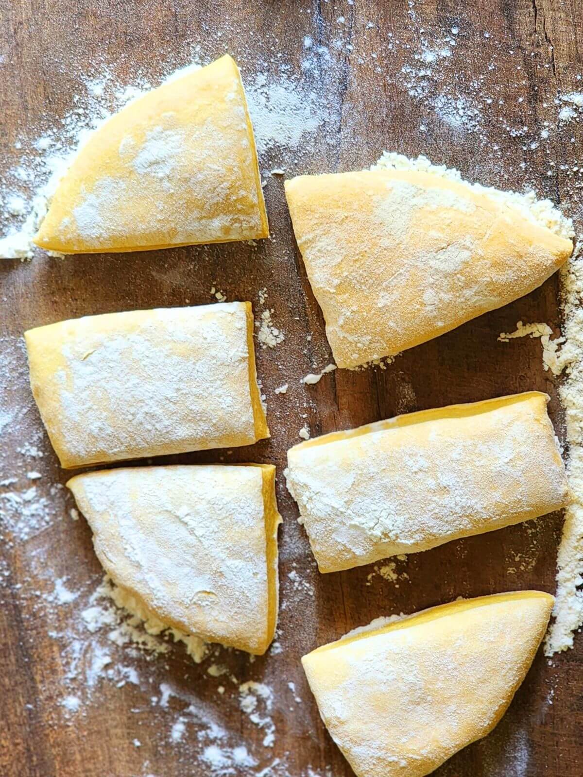 Homemade pumpkin pasta dough divided into six floured pieces on a wooden work surface.