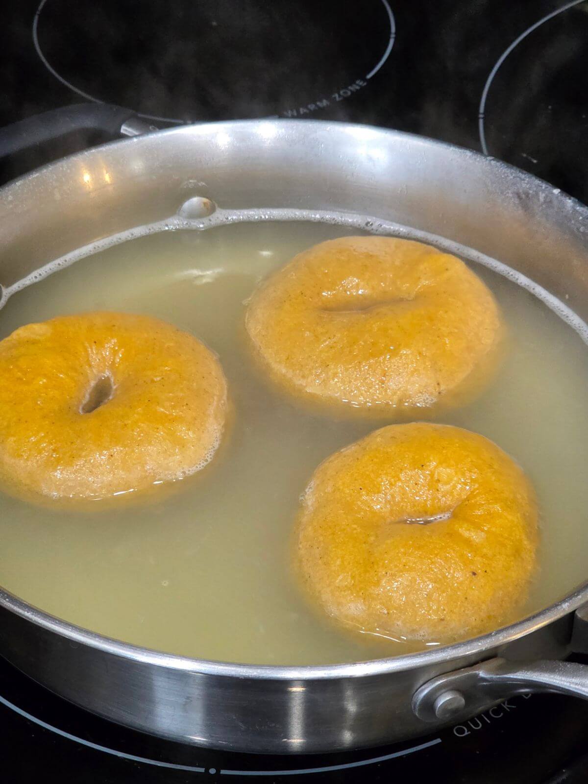 Sourdough pumpkin bagels boiling in water before baking.