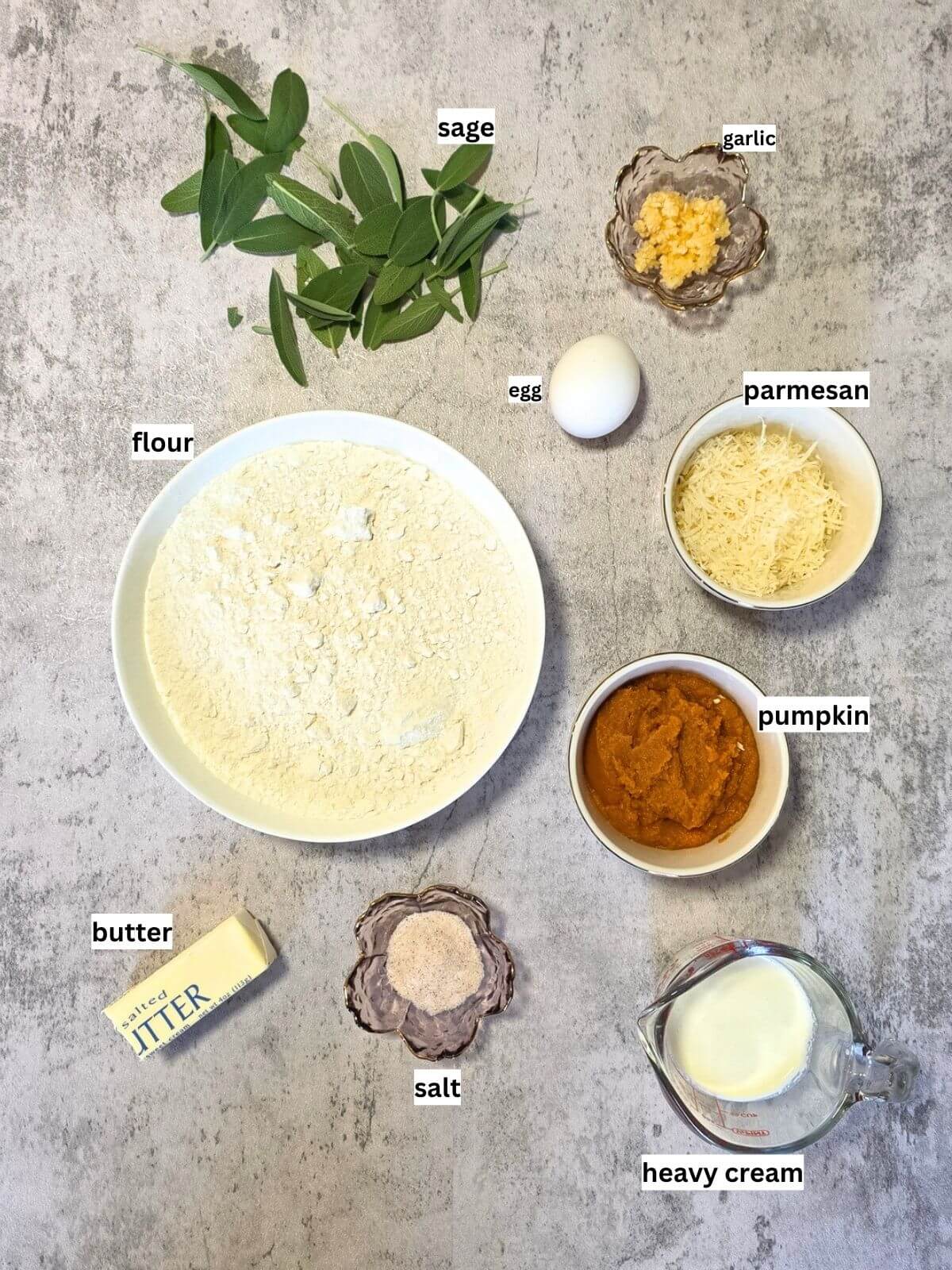 Ingredients for homemade pumpkin pasta with sage butter sauce, including flour, pumpkin puree, egg, butter, sage, garlic, Parmesan and heavy cream.