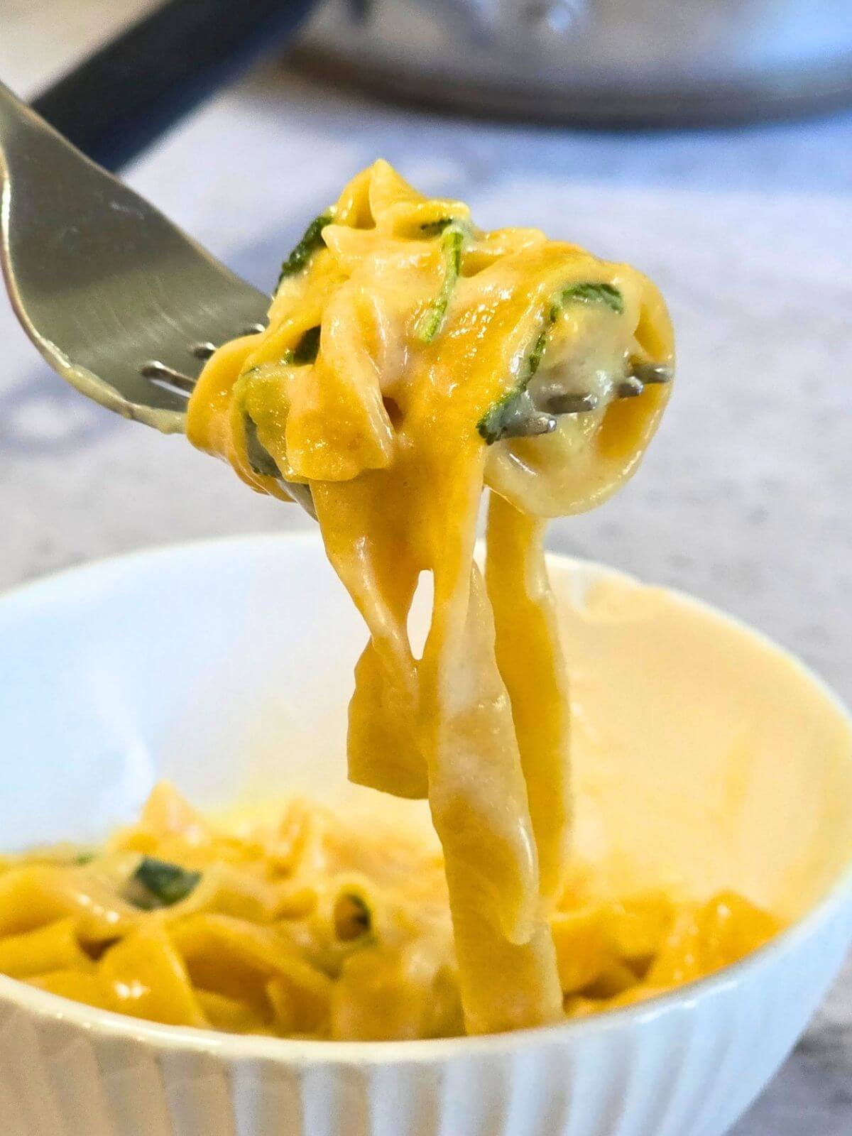 Forkful of homemade pumpkin pasta with creamy sage butter sauce and fresh sage.