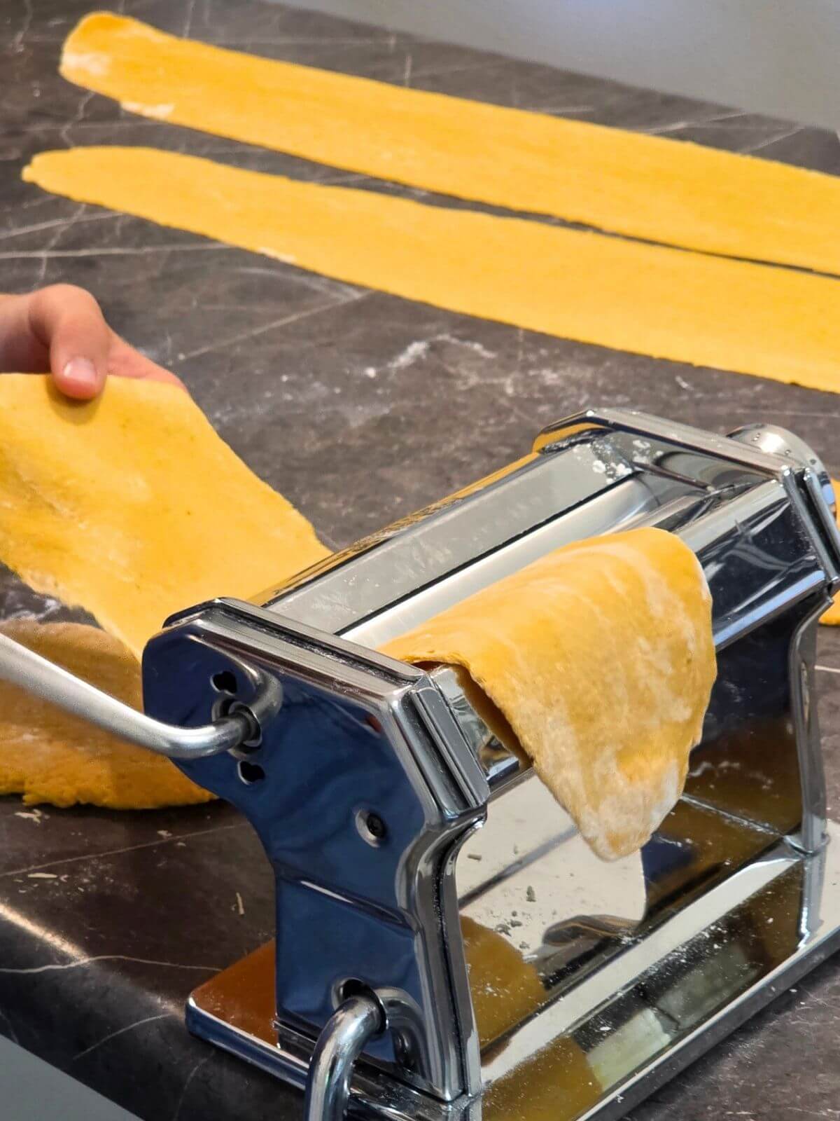 Pumpkin pasta dough being rolled into thin sheets with a hand crank pasta machine.