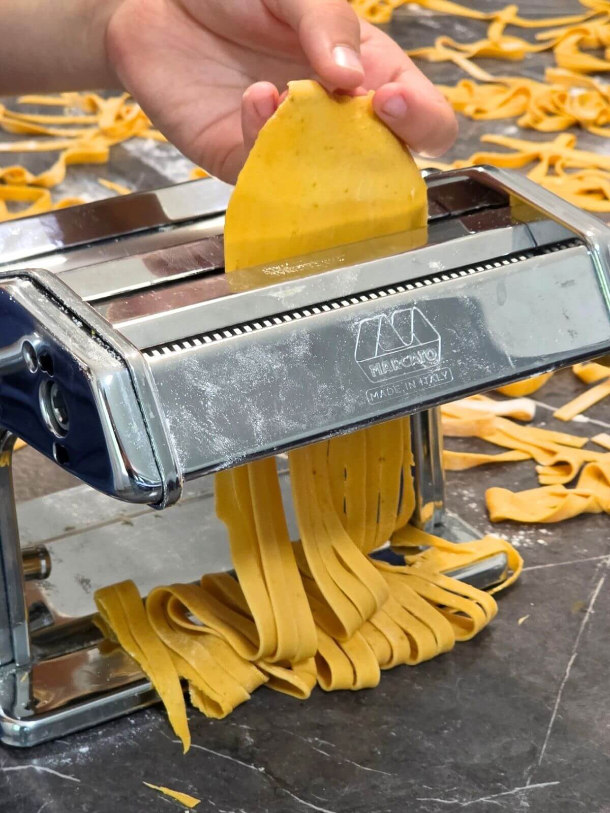 Fresh pumpkin pasta being cut into fettuccine noodles with a pasta machine.