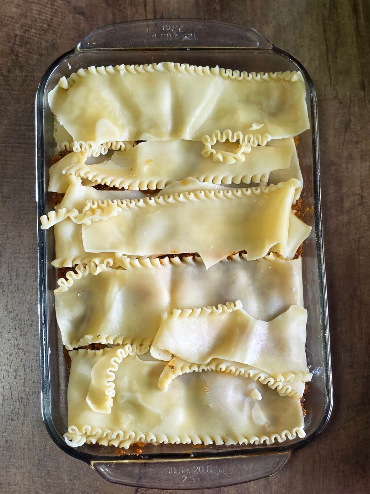 Lasagna noodle layered on meat sauce in a clear baking dish. 