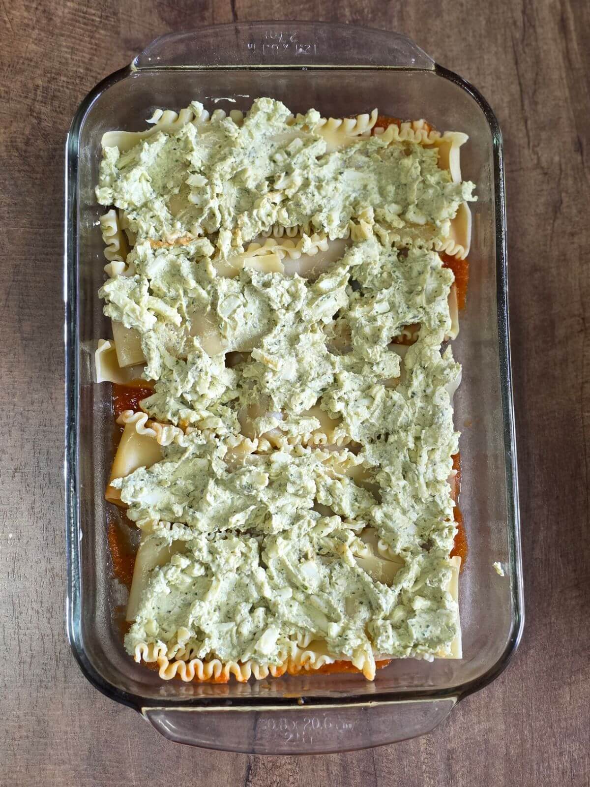 Pesto ricotta layered on lasagna noodle in a glass baking dish.