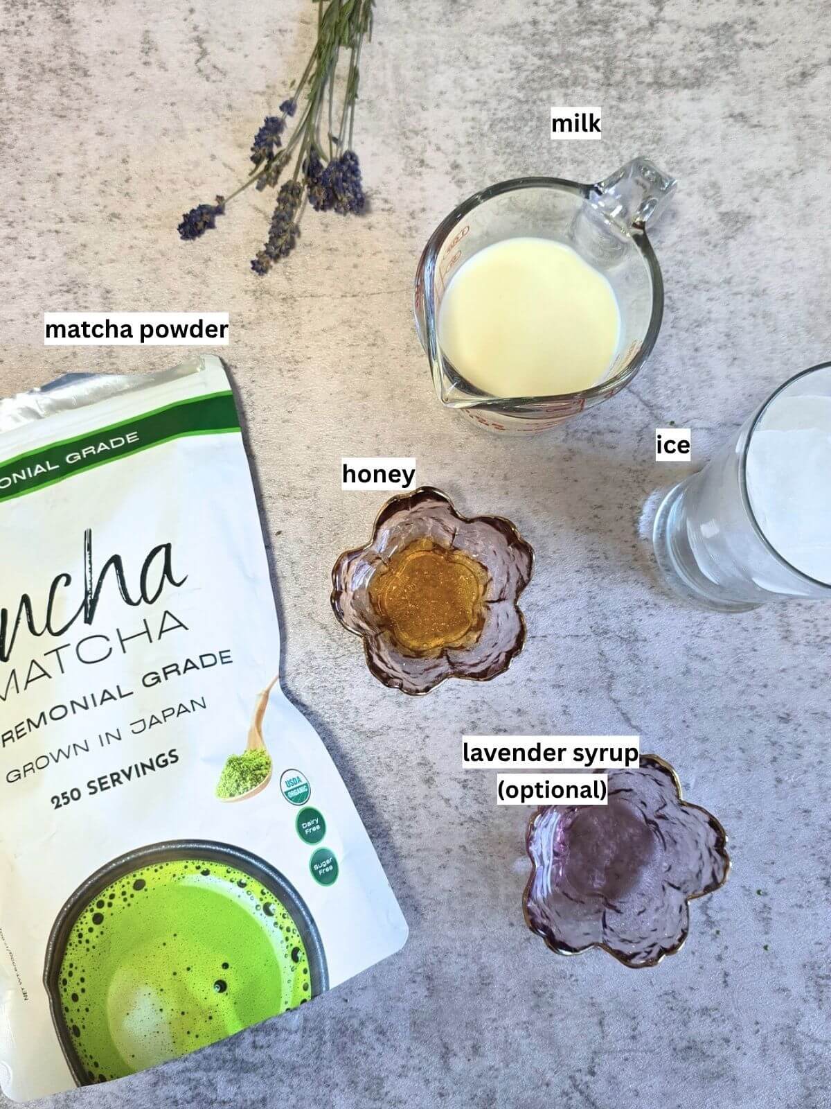 Ingredients for an iced matcha latte including ceremonial grade matcha powder, milk, honey, lavender syrup and ice.