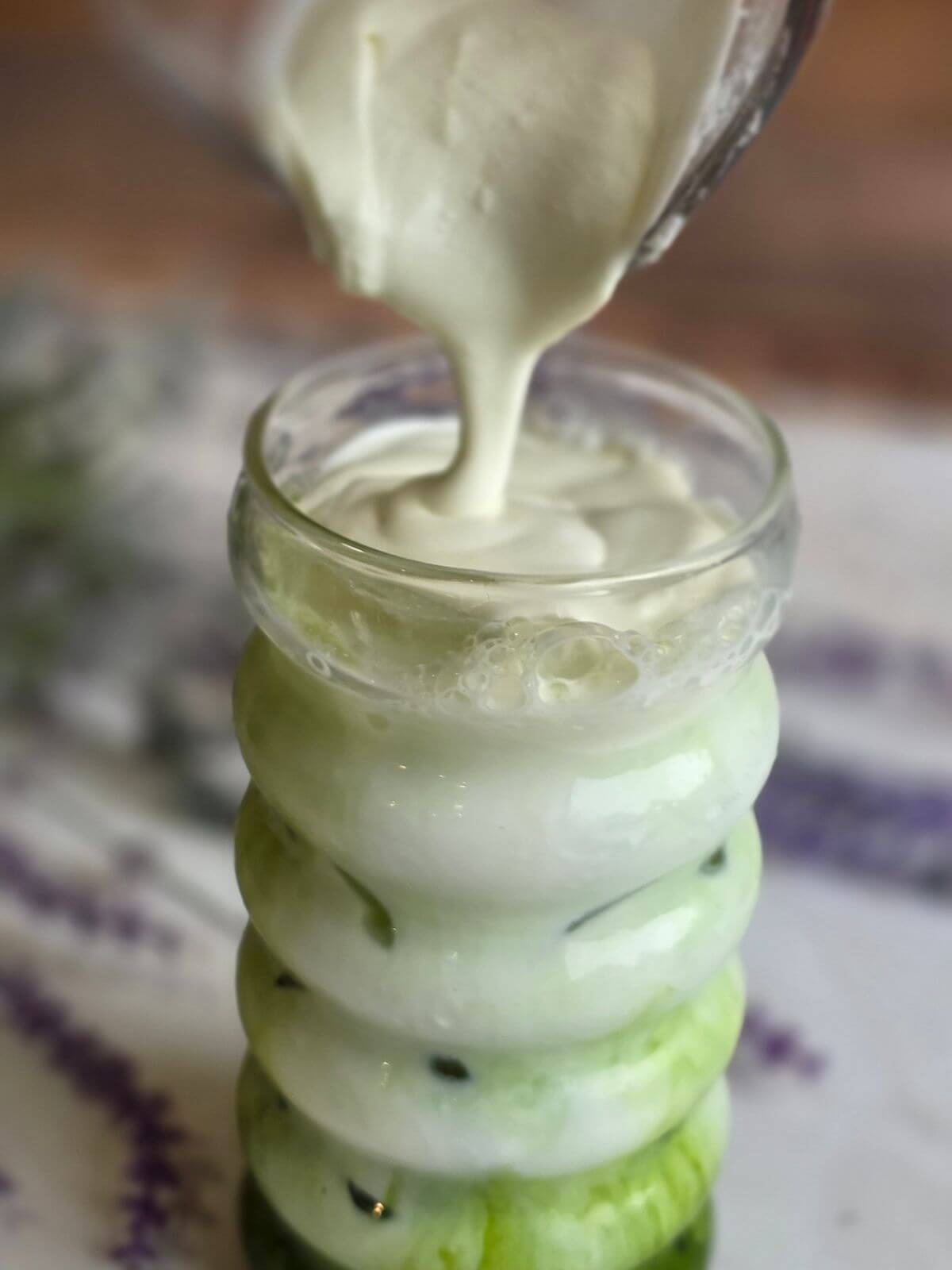 Homemade cold foam being poured over an iced matcha latte.