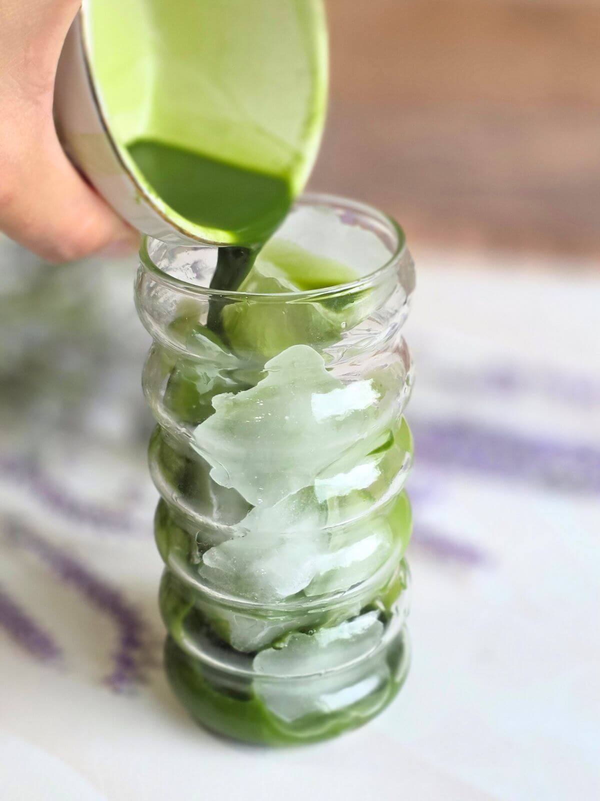 Whisked matcha being poured over a glass filled with ice.
