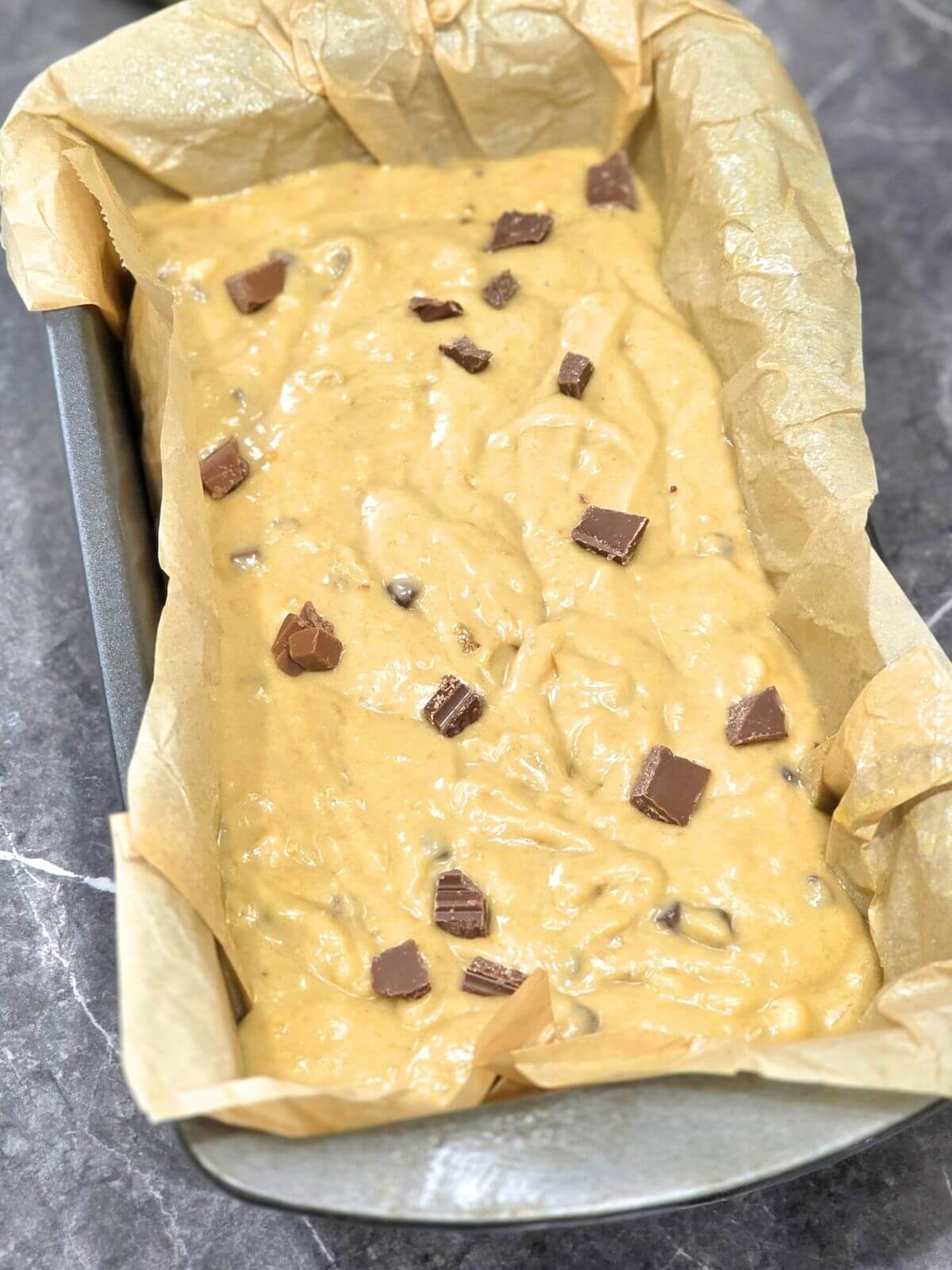 Sourdough chocolate chip banana bread batter in a parchment lined loaf pan before baking