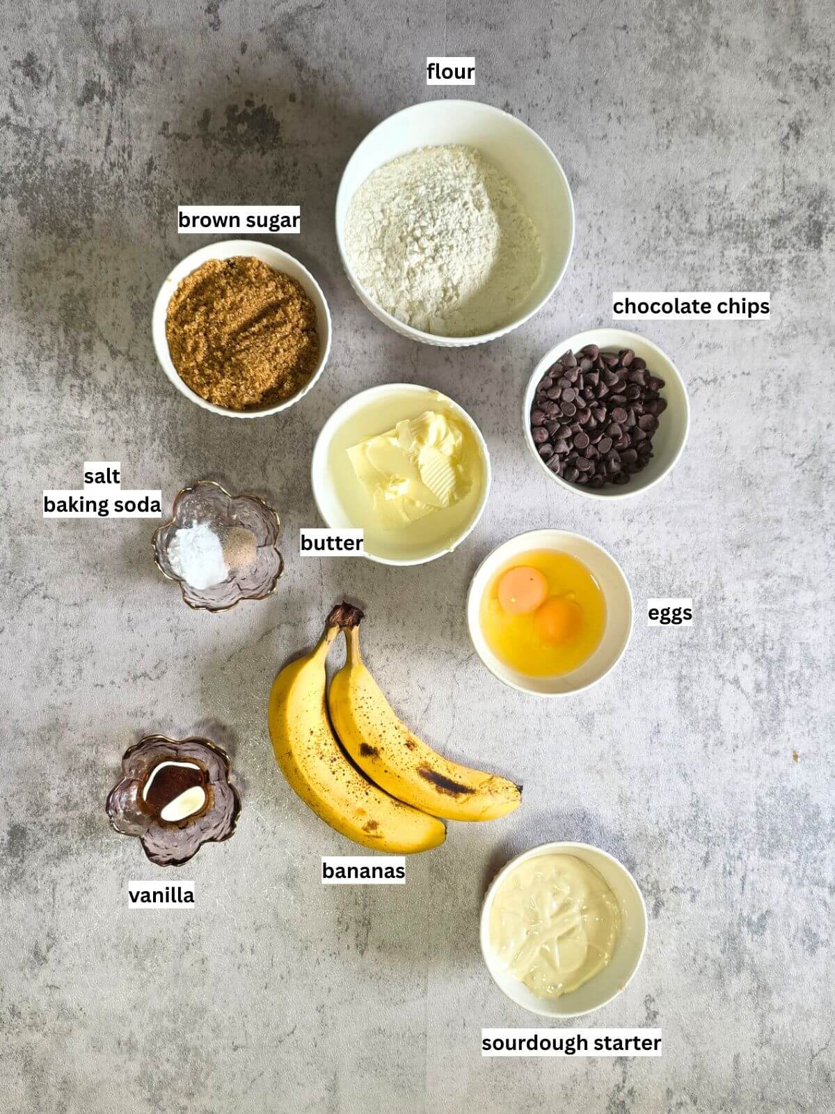 Ingredients for sourdough discard banana bread with ripe bananas, sourdough starter, flour, brown sugar, eggs, butter, and chocolate chips.