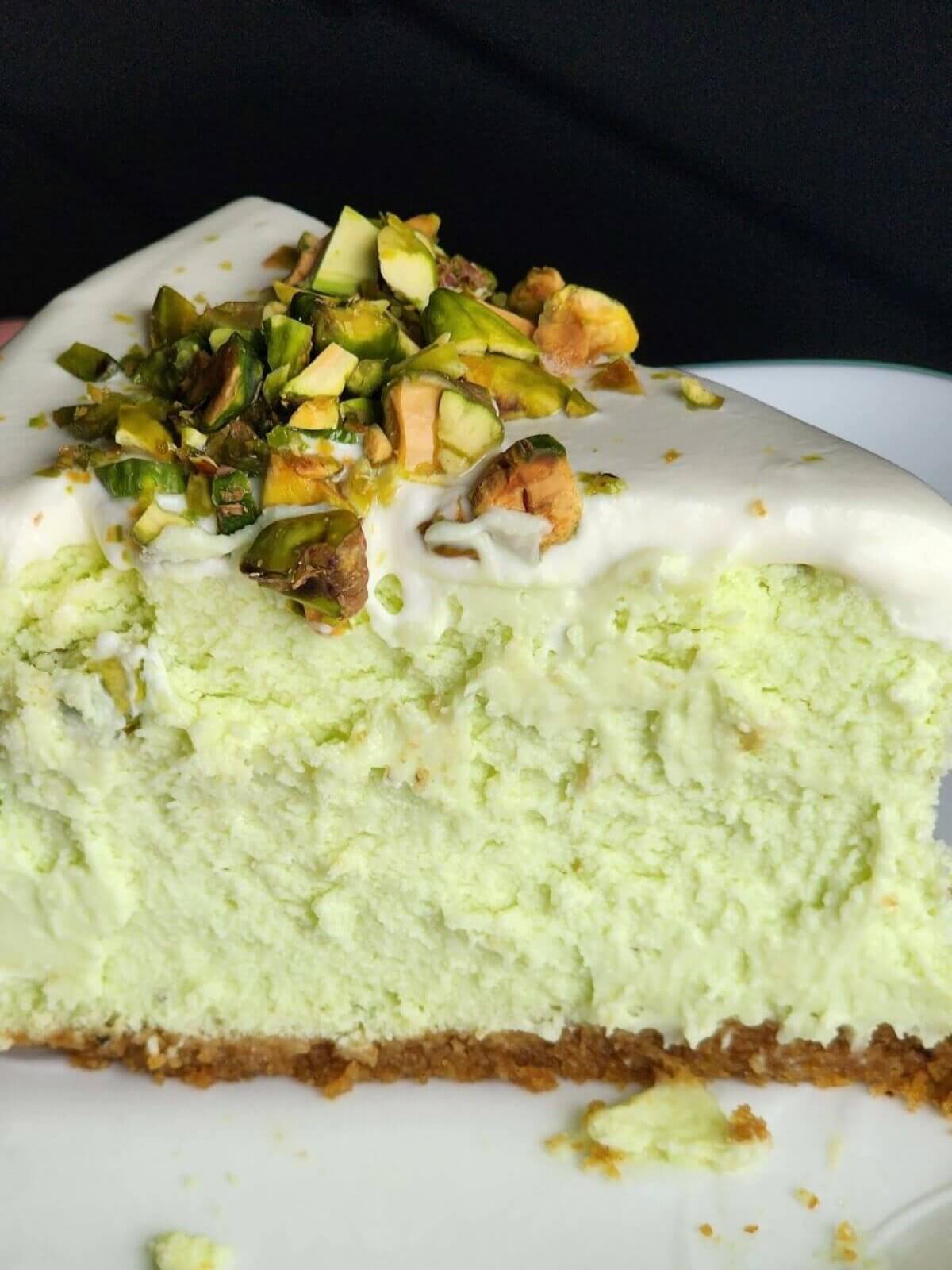 Slice of pistachio cheesecake with sour cream icing and chopped pistachios.